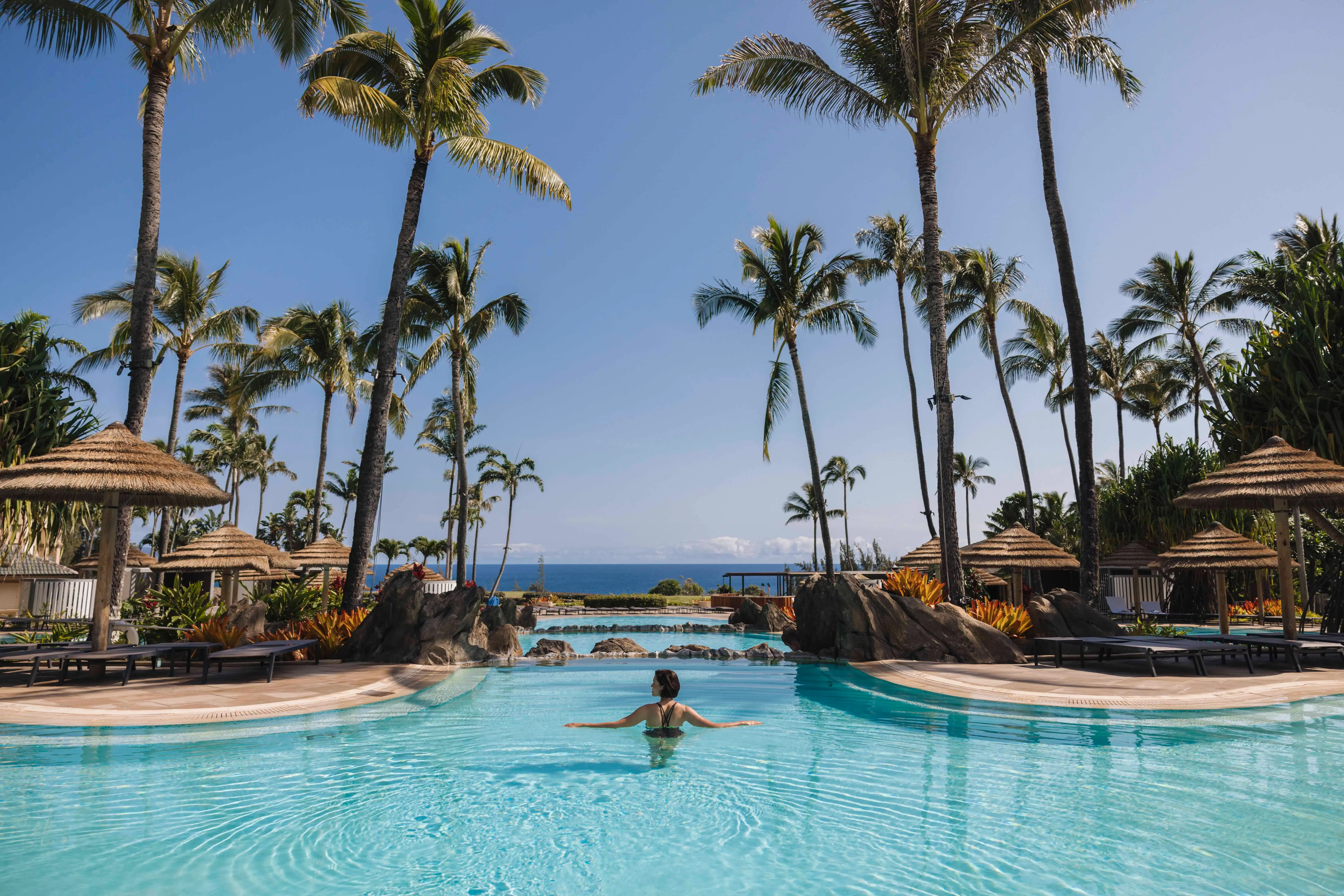 A guest of The Ritz-Carlton Maui, Kapalua swimming down the middle of the adults only pool between thatched sun umbrellas and palm trees