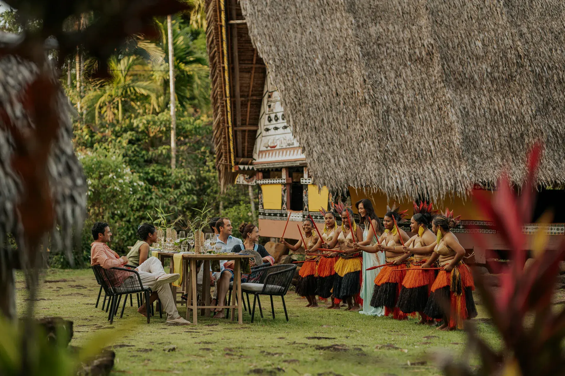 A group of Four Seasons Explorer Palau guests enjoying a cultural performance in front of a traditional Bai house