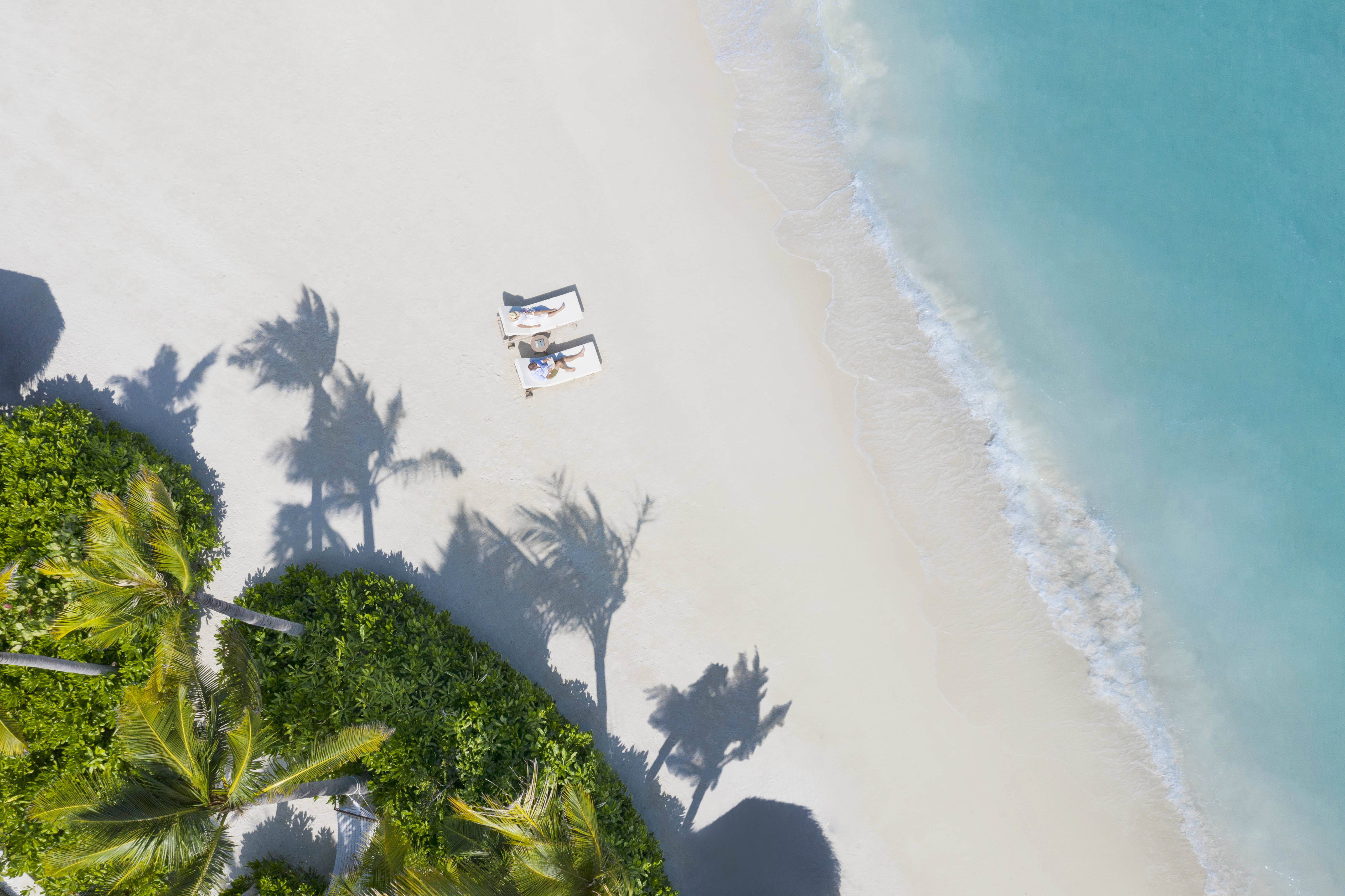 Man and woman on lone sun loungers on white sand beach 