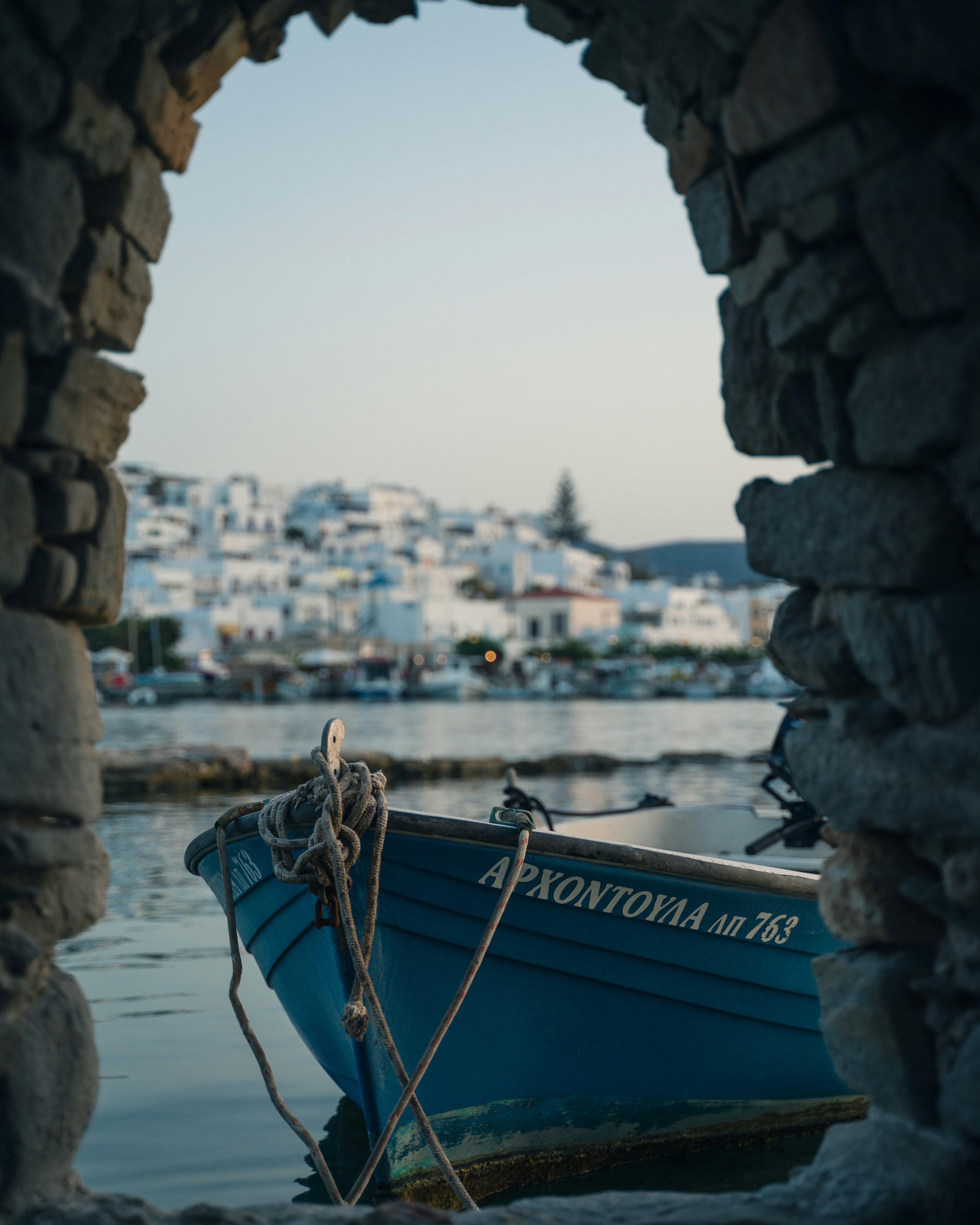 Blue boat moored up under an arch in Naoussa in Paros with buildings of the town behind