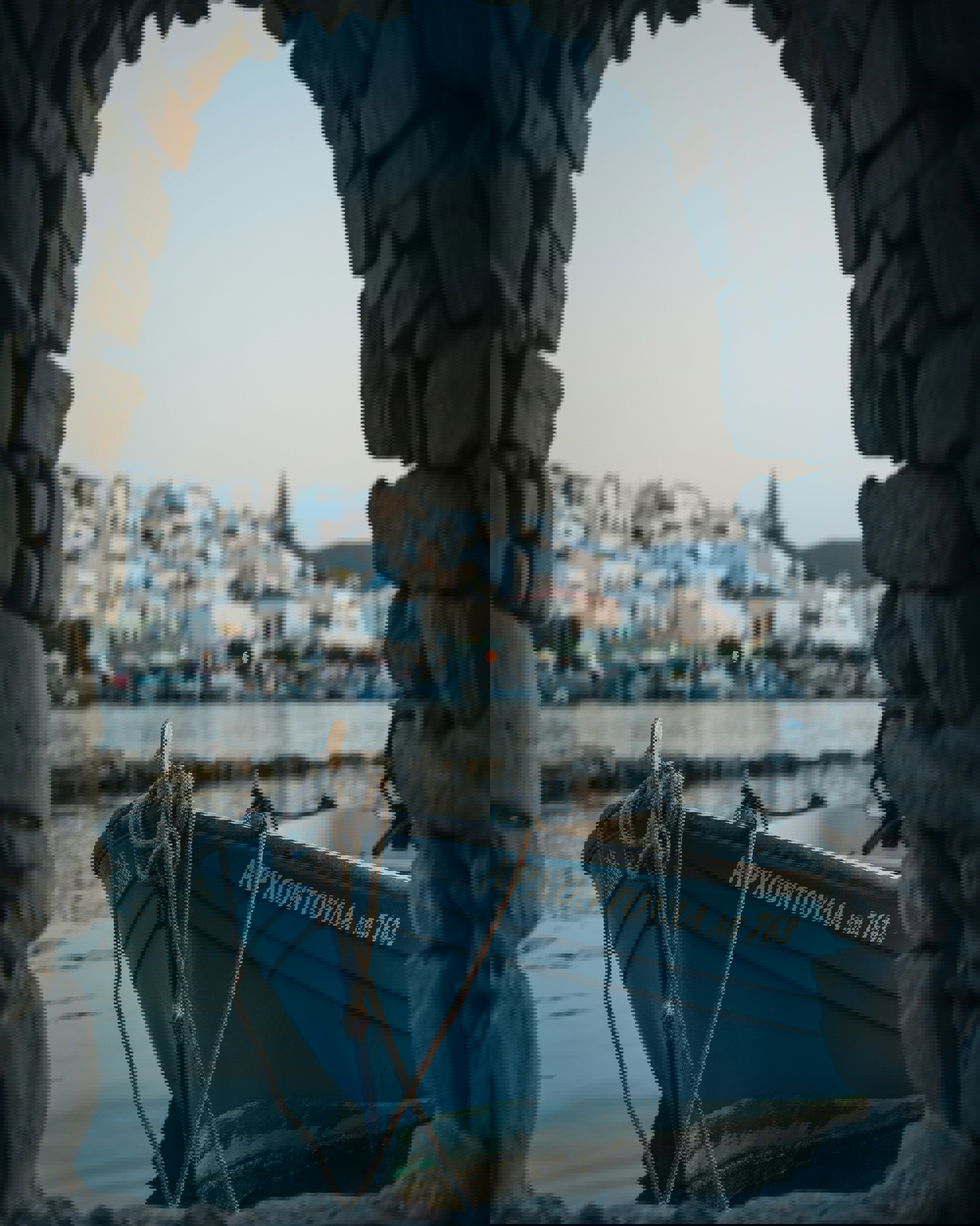 Blue boat moored up under an arch in Naoussa in Paros with buildings of the town behind