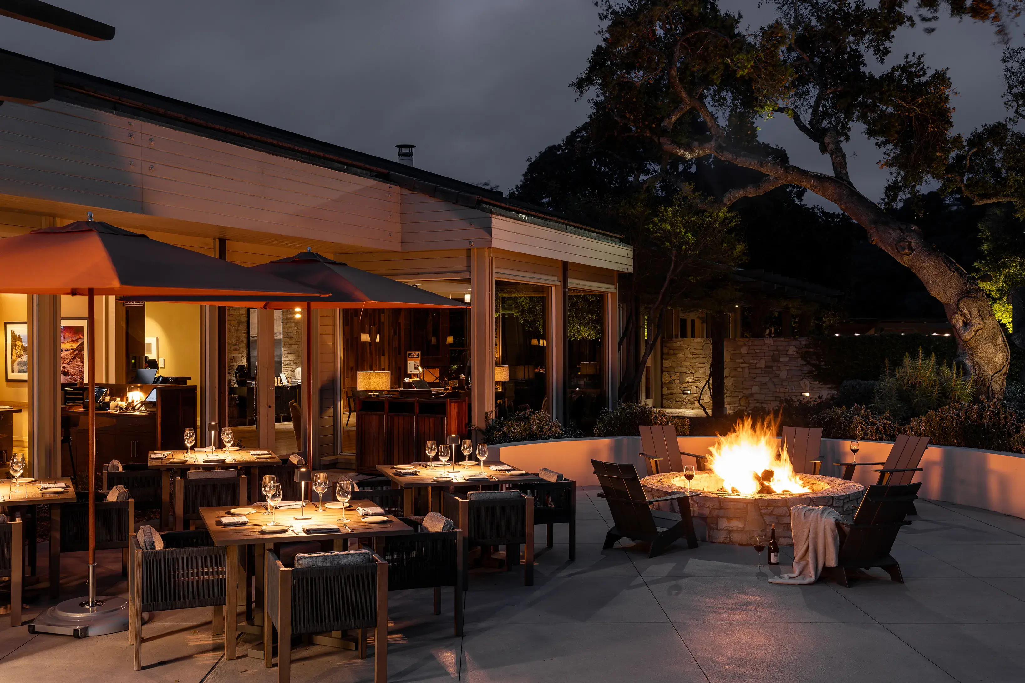 The kitchen patio at Carmel Valley Ranch in California at night featuring a cosy firepit with wine and blankets and tables set for dinner