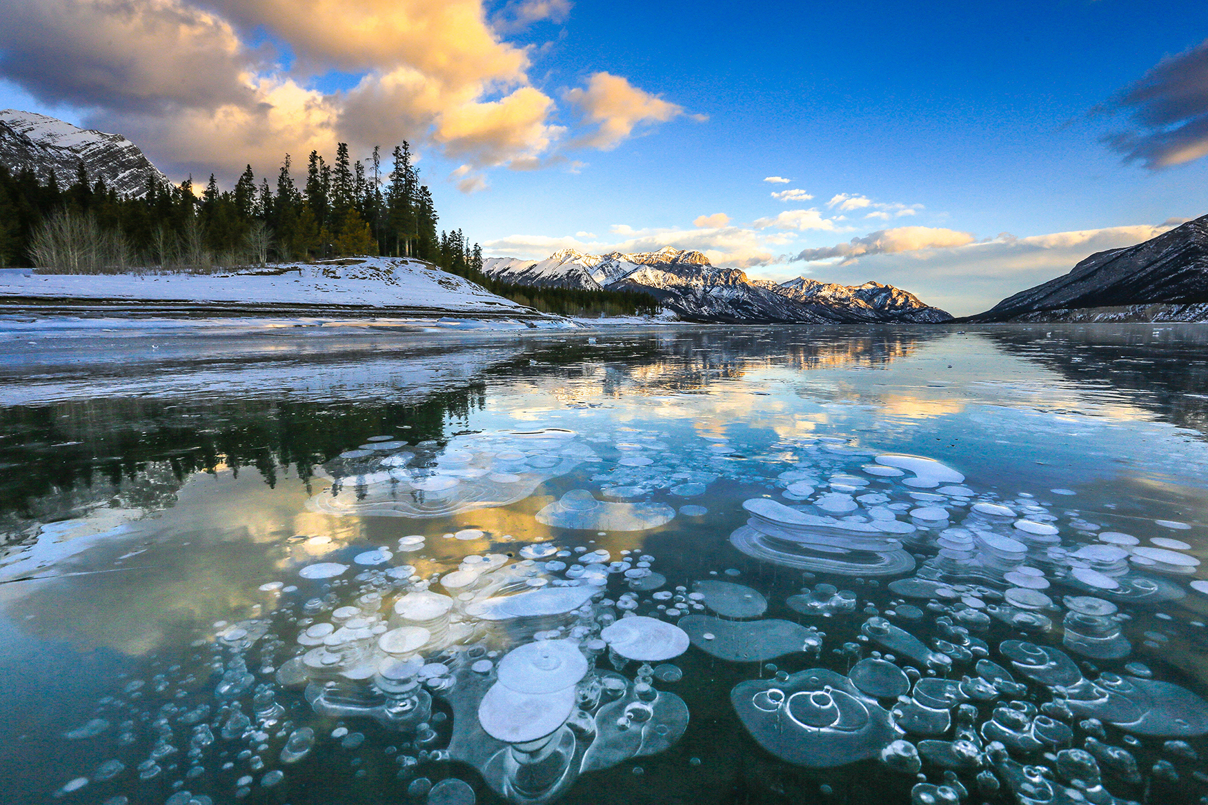 Frozen bubbles of Abraham Lake in Canada backed by sun-lit mountains