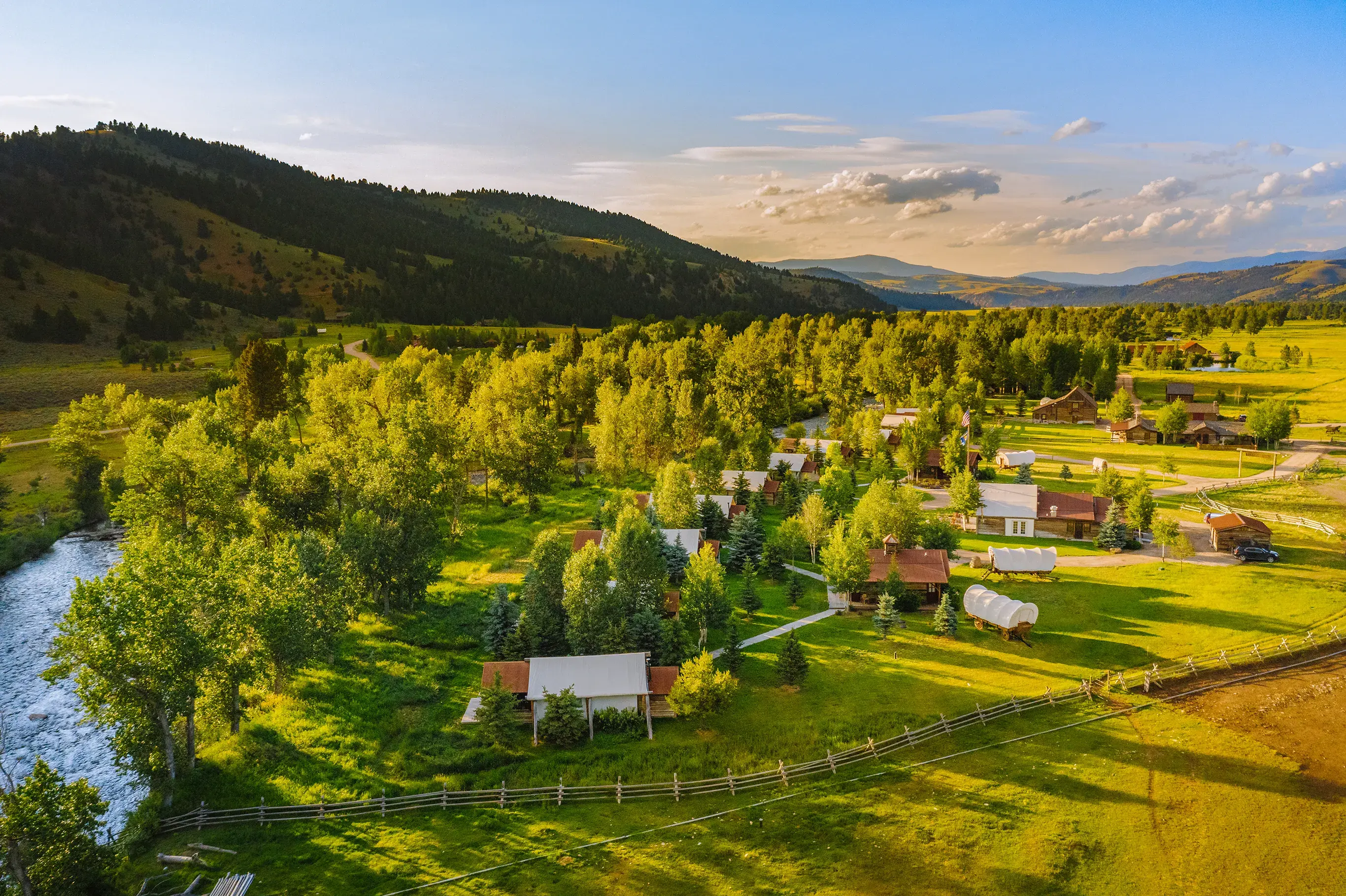 Aerial shot of The Ranch at Rock Creek in Montana featuring canvas and wooden cabins set among trees beside a river backed by mountains