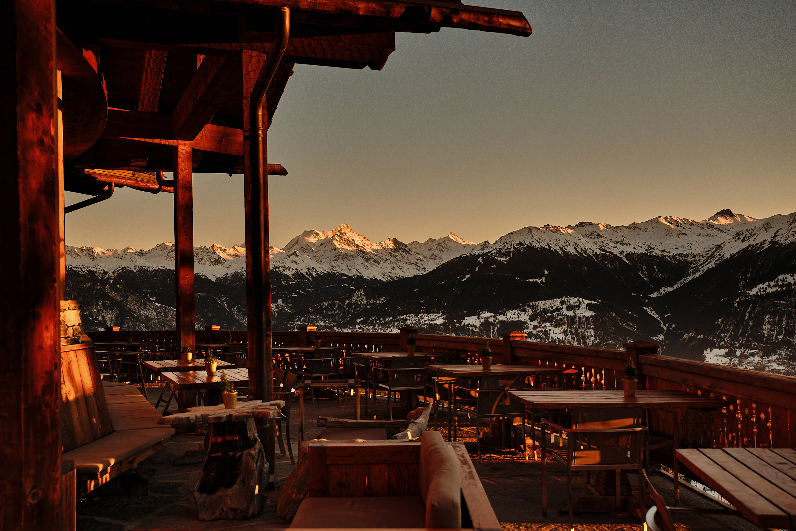 The outdoor dining terrace of LeCrans lit but sunset light facing the snowy mountains