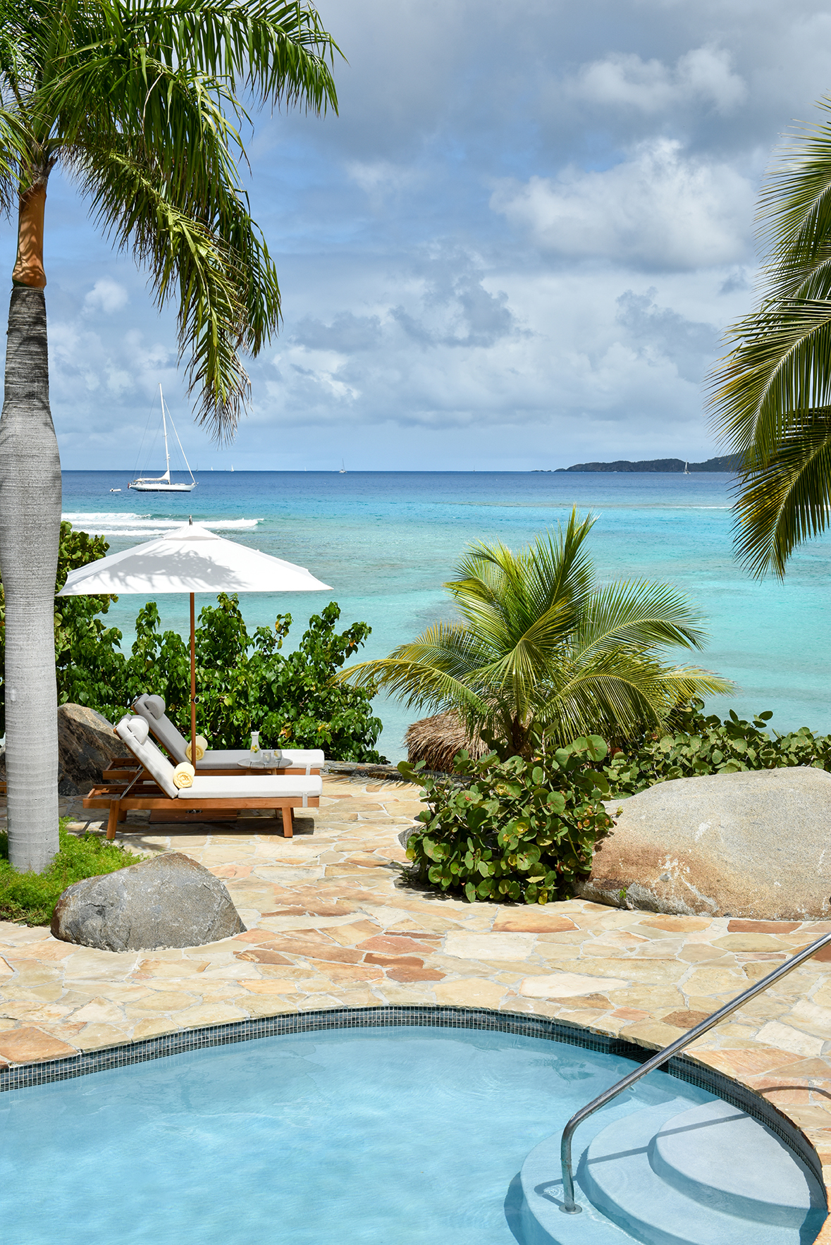 Caribbean & Mexico, British Virgin Islands, Virgin Gorda, Rosewood Little Dix Bay, pool and sunloungers with view of yacht on sea
