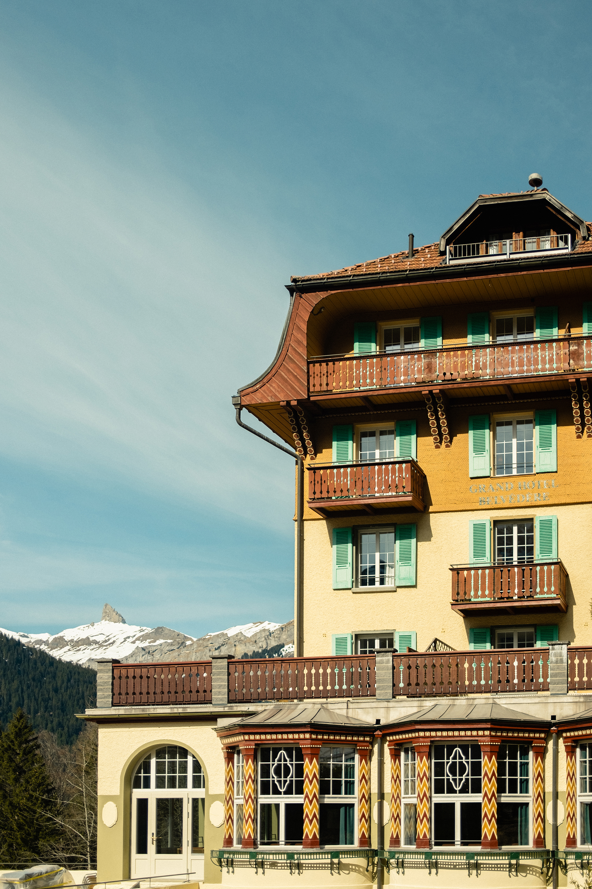 The detailed exterior of Grand Hotel Belvedere featuring wooden balconies, green shutters and patterned columns, with a clear sky behind