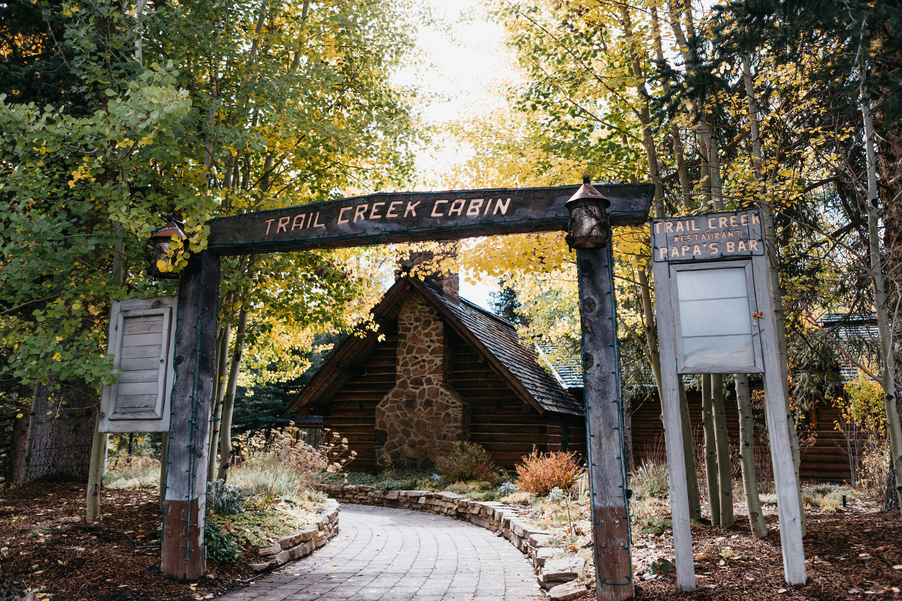 Entrance to Trail Creek Cabin with a wooden archway and a stone path leading to a rustic cabin surrounded by trees