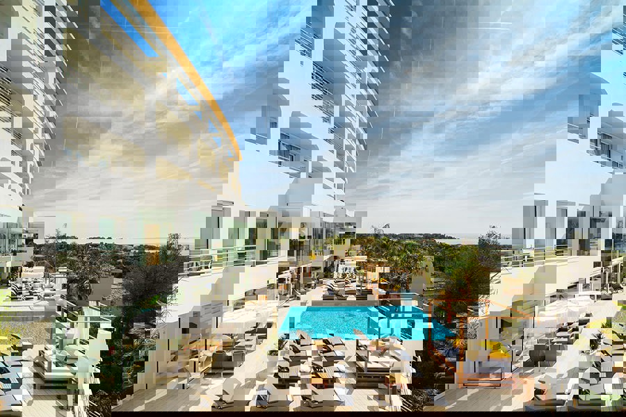 Modern luxury hotel at Portals Hills in Mallorca with a large outdoor pool, sun loungers, and cabanas under a clear blue sky.