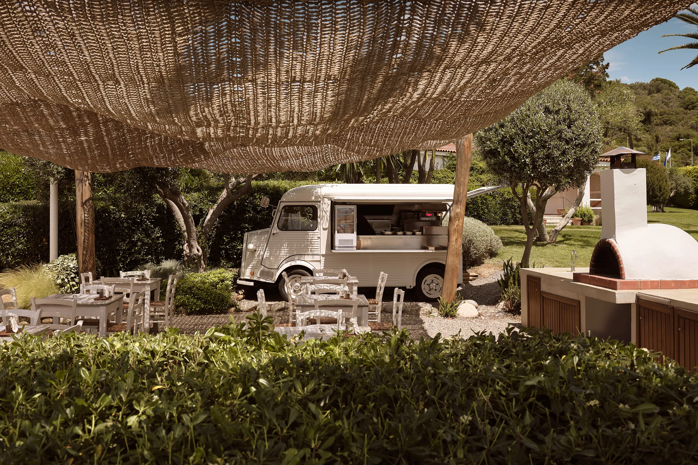 Outdoor garden dining area at Eagles Palace in Greece featuring a charming vintage food truck under woven shade.