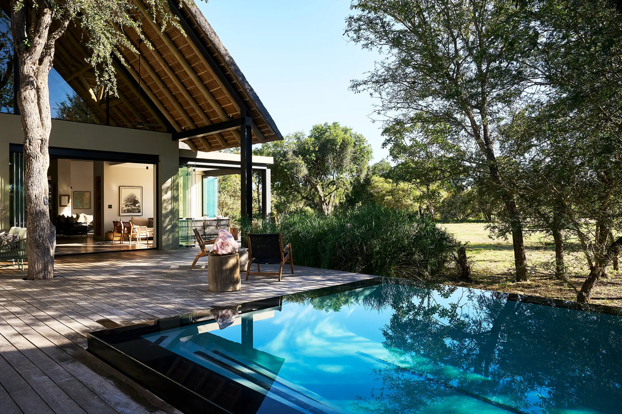 An outdoor area at Monwana Game Reserve featuring a deep infinity swimming pool on the terrace with chairs set up beside and a glimpse of an indoor lounge behind, facing the open landscape