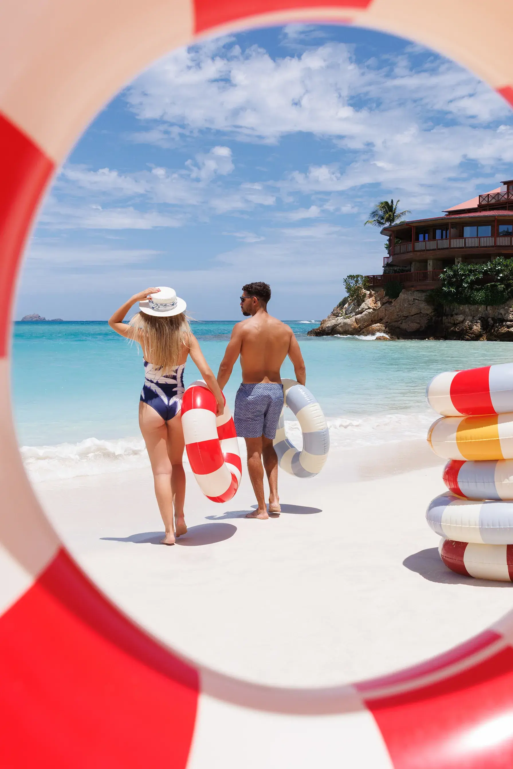 A couple walking towards the ocean on a white sand beach with colourful inflatable rings