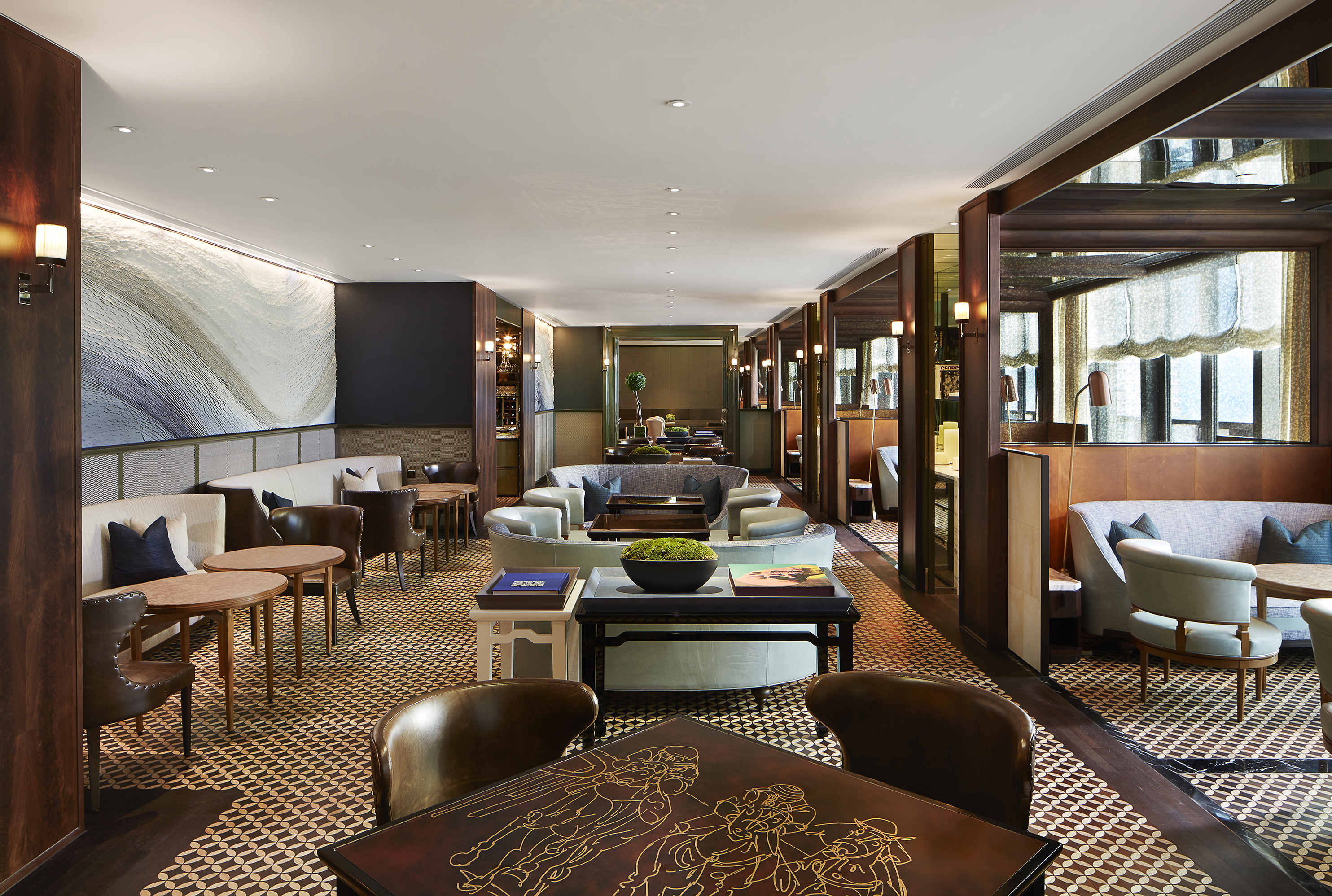 The lounge of the Manor Club at Rosewood Hong Kong featuirng lots of comfy tables and chairs in deep warm neutral tones and dark wood accents