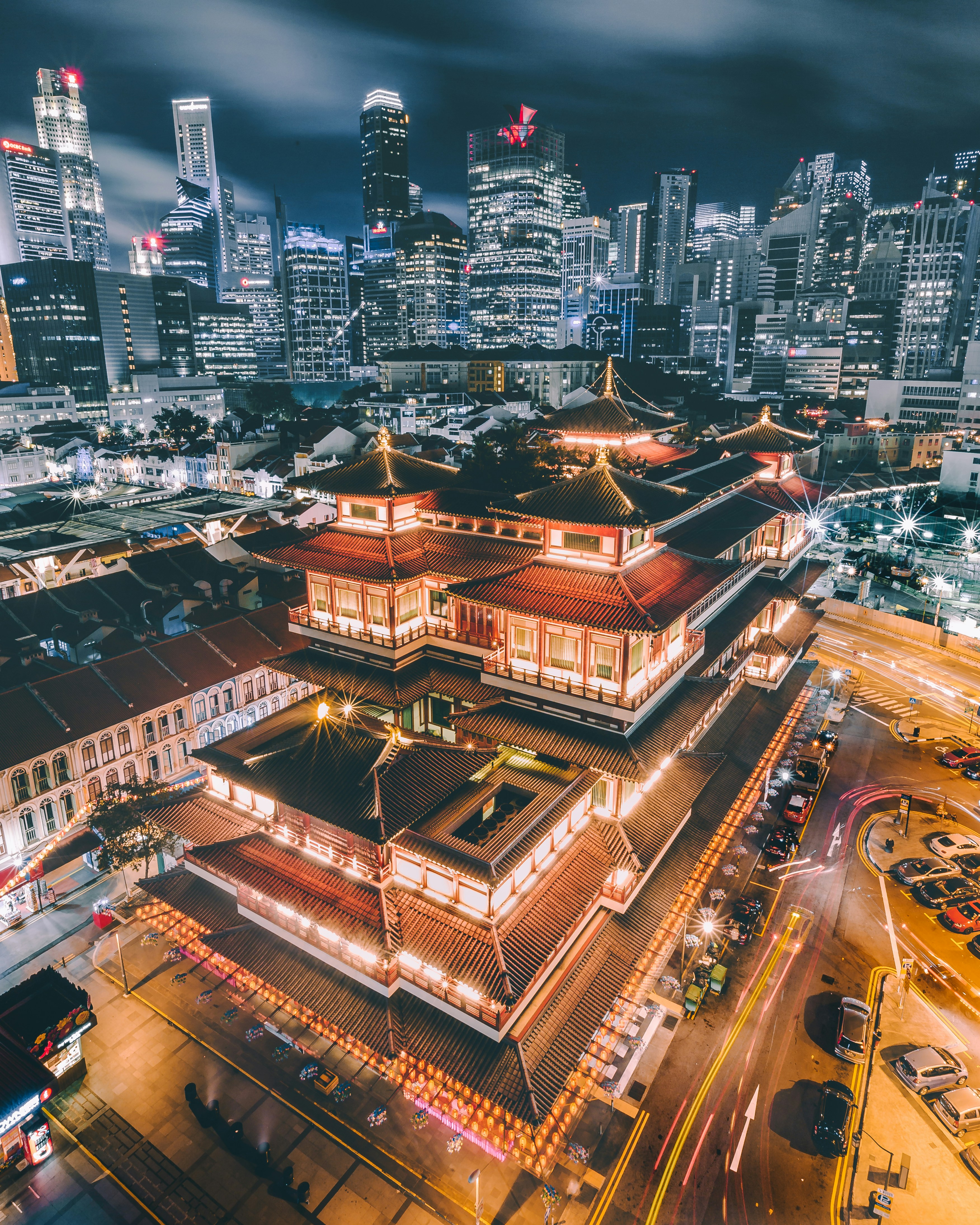 The Budha Tooth Relic Temple in Singapore lit up at night with the city skyline in the background