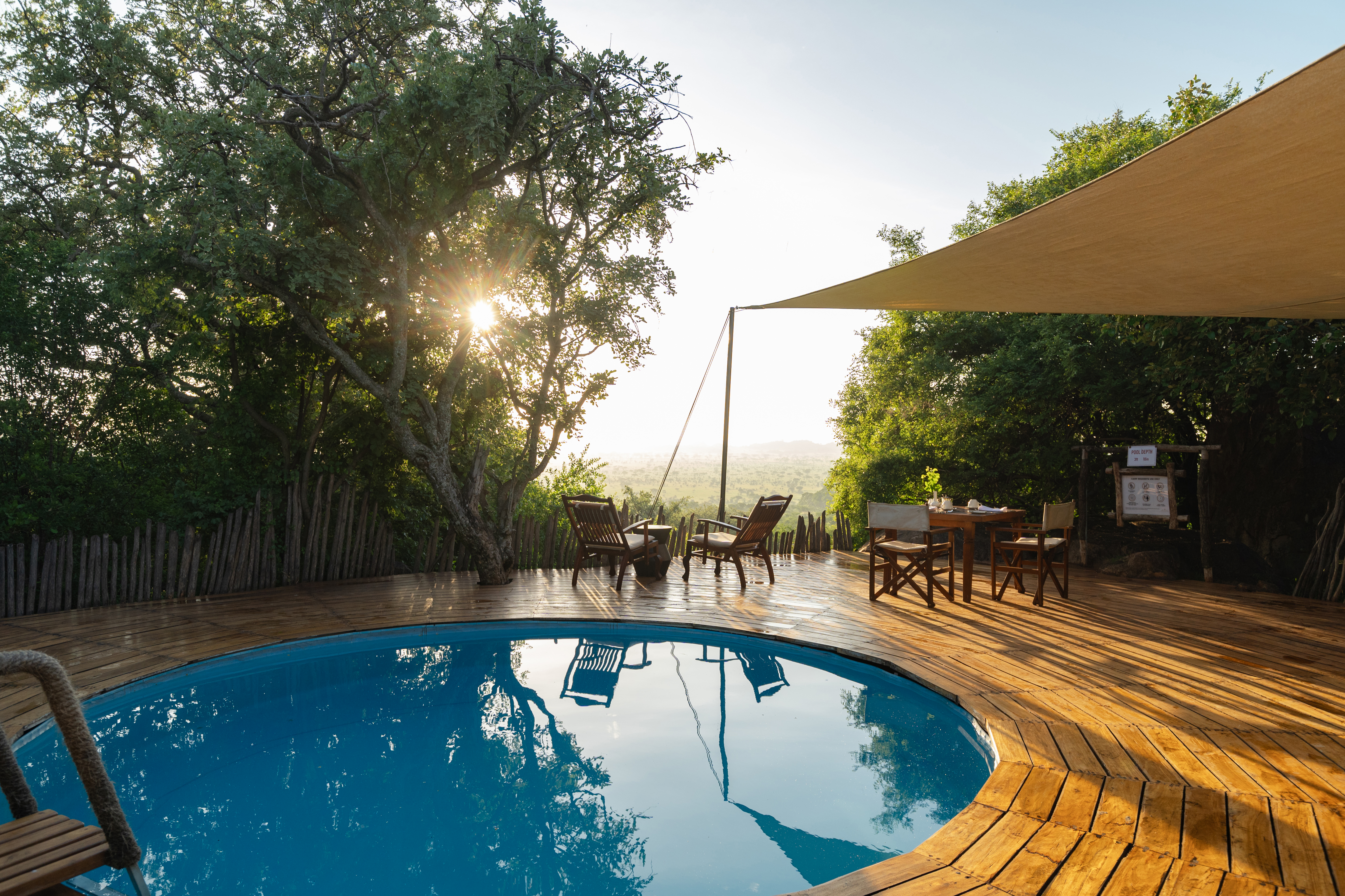 A circular pool surrounded by a wooden terrace with furniture and a canvas canopy looking out over the landscape- at Elewana Serengeti Pioneer Camp