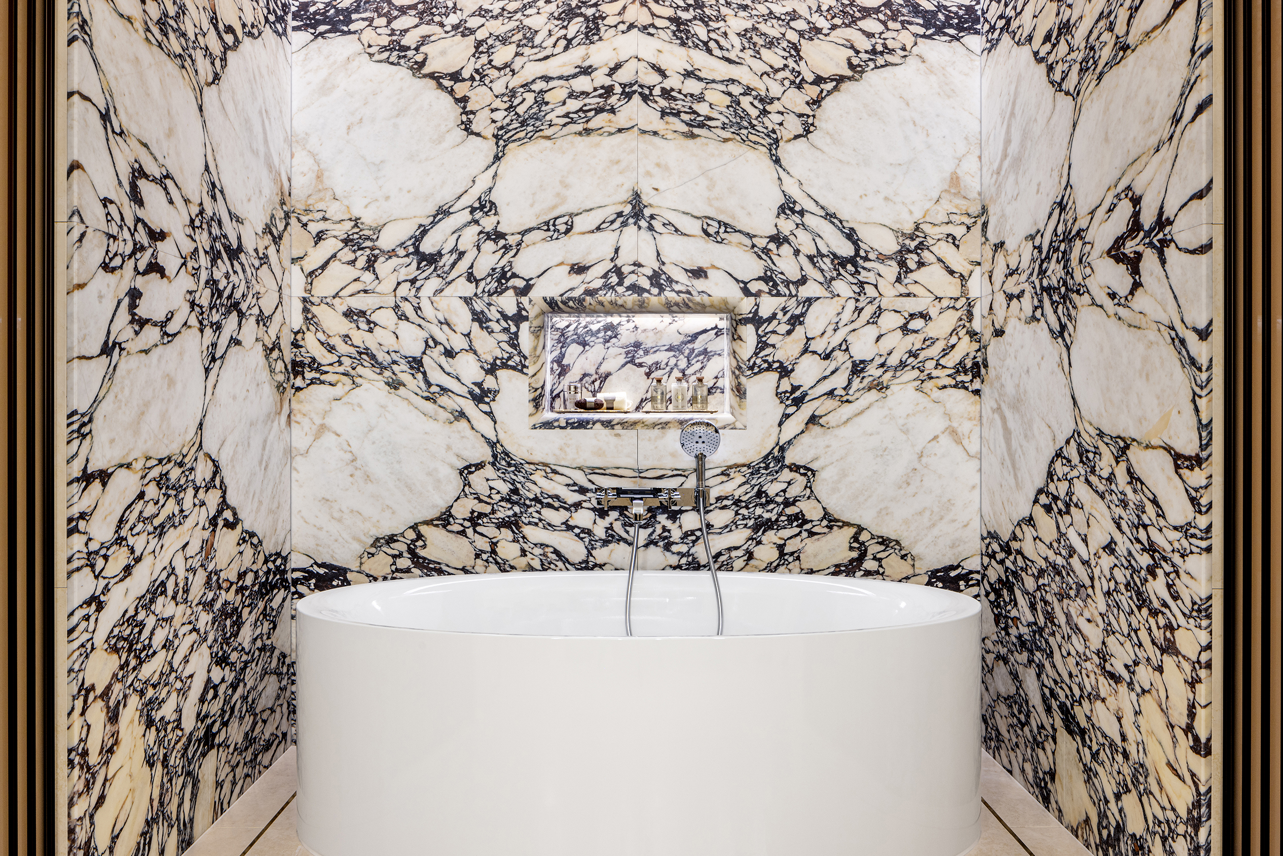 A sleek oval bathtub in a marble-walled alcove