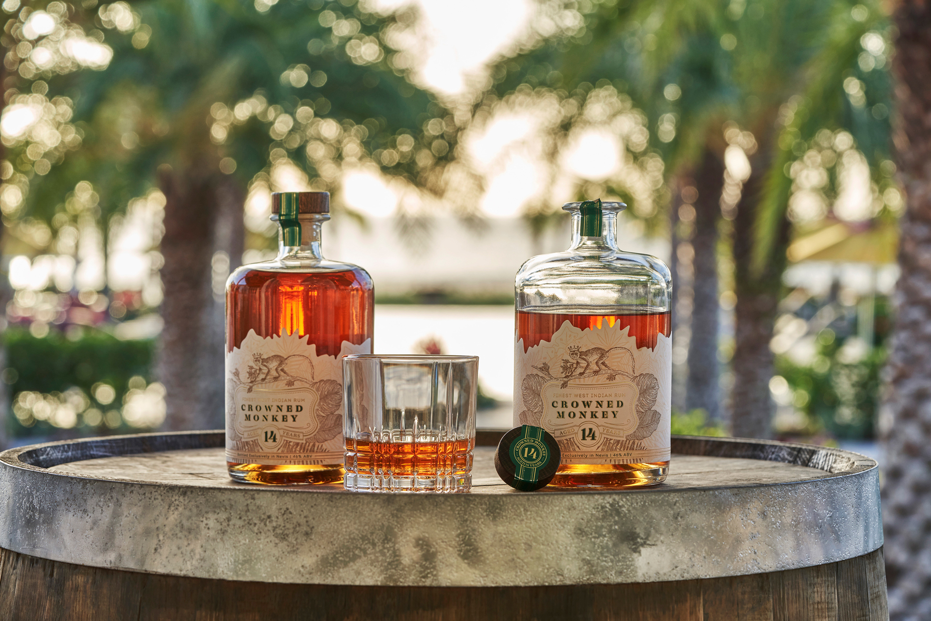 A half full glass situated between two bottles of crowned monkey rum