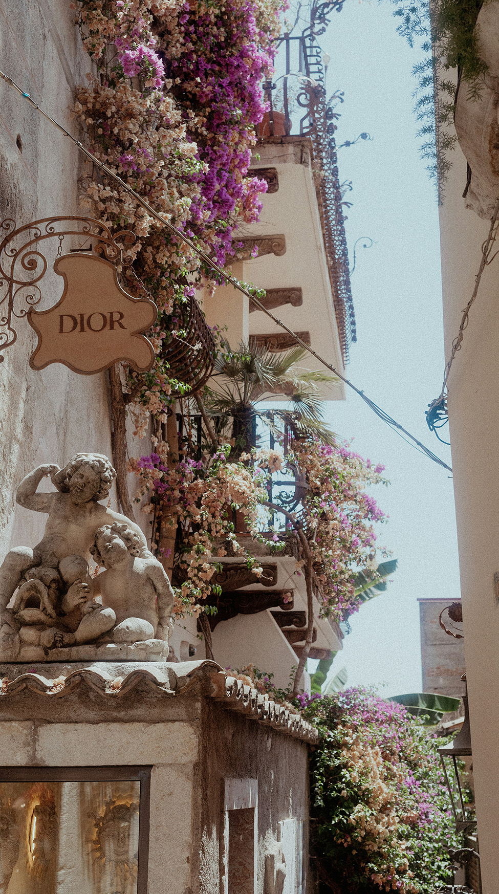 Europe, Italy, Sicily, street with balconies and pruple flowers with a Dior shop sign and a statue