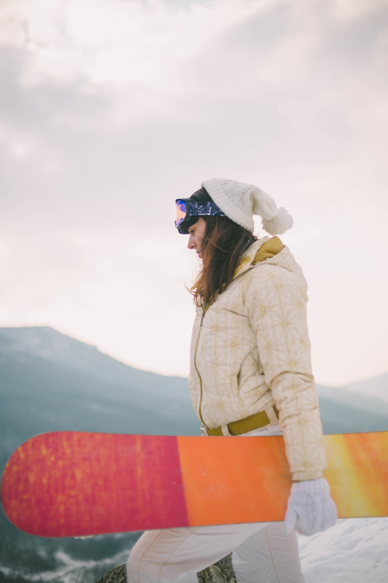 Woman holding snowboard with mountains in background