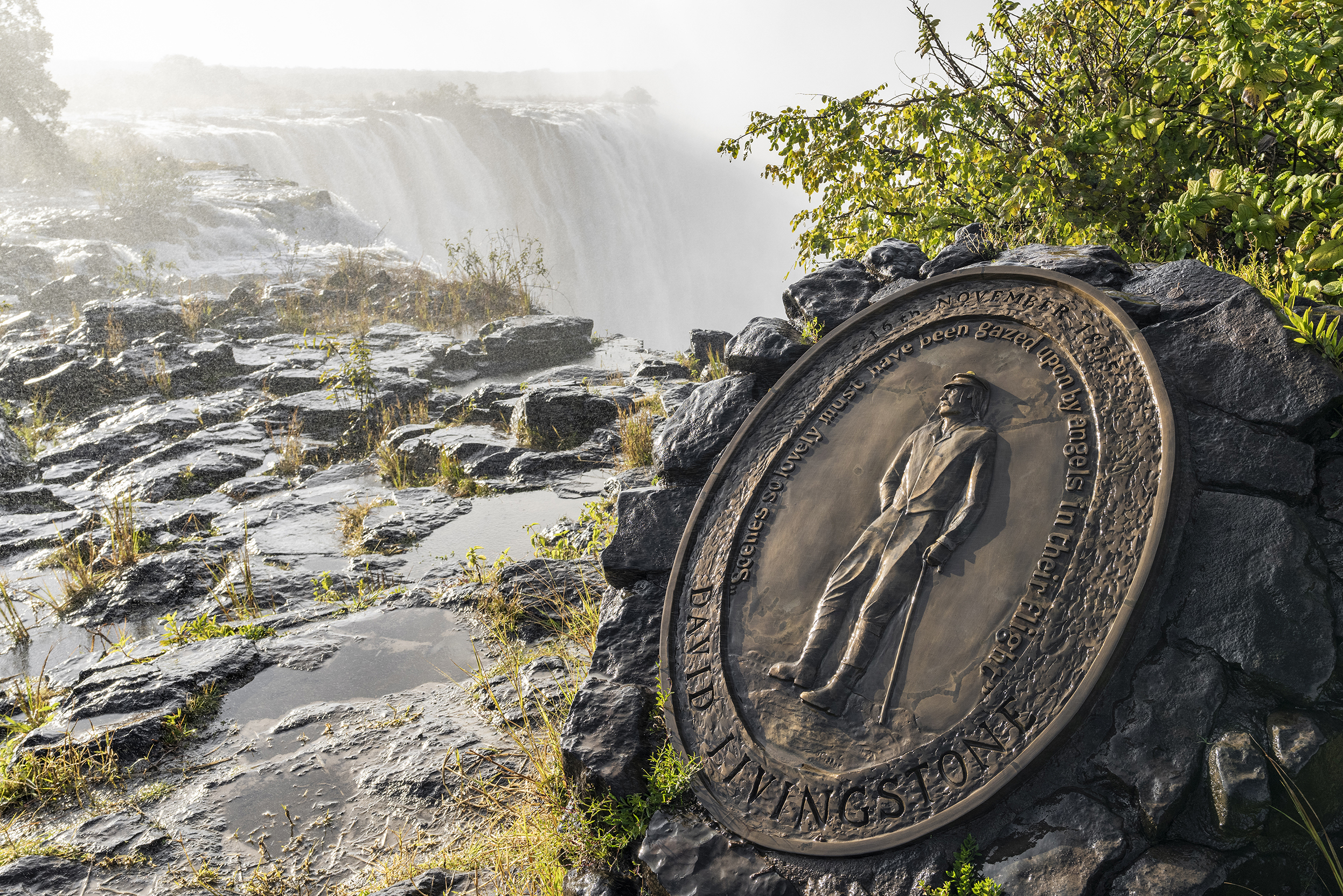 David Livingstone memorial plaque near Victoria Falls with mist and lush greenery in the background.
