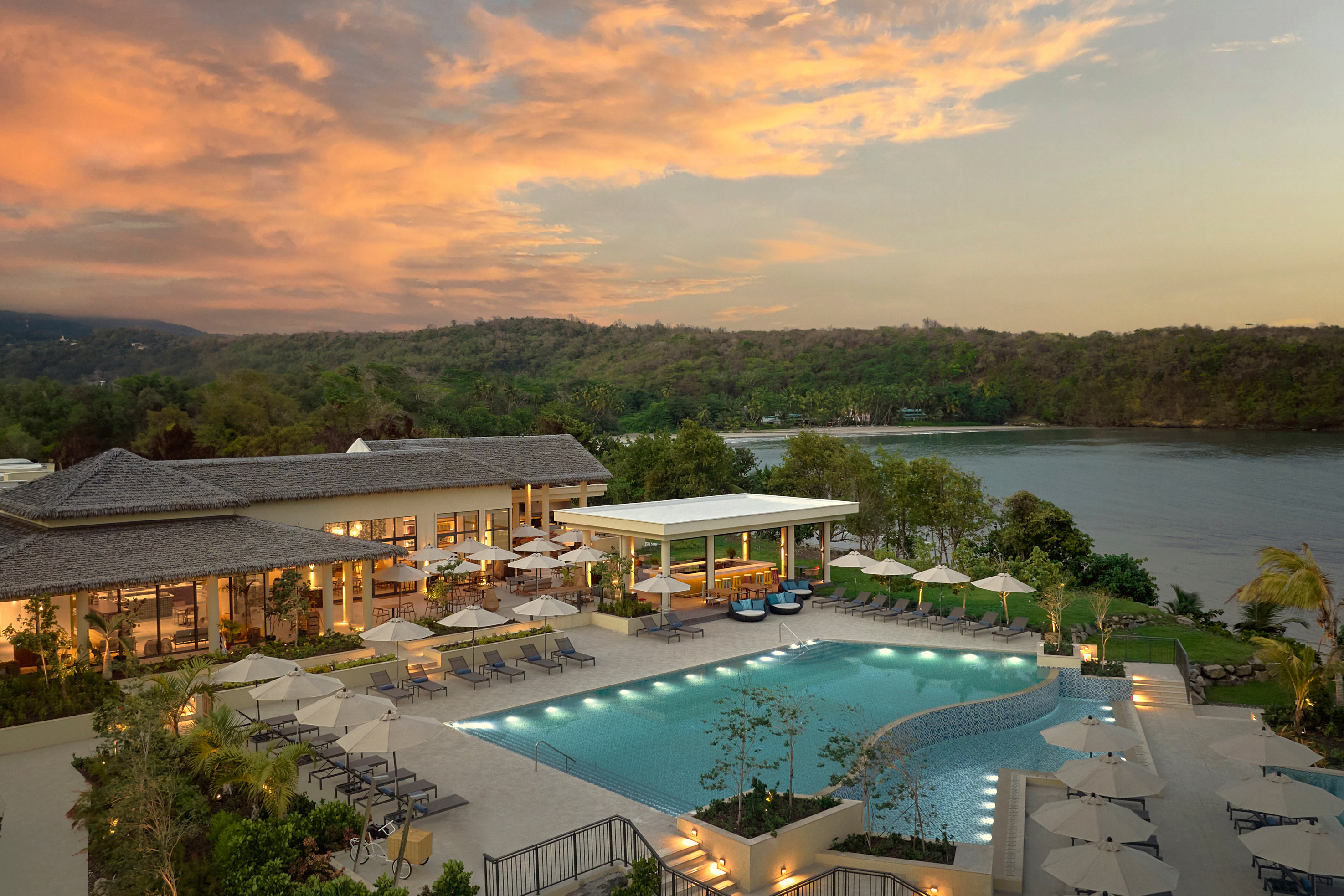 A large outdoor pool flanked by parasols and lounge chairs sits right on the shoreline