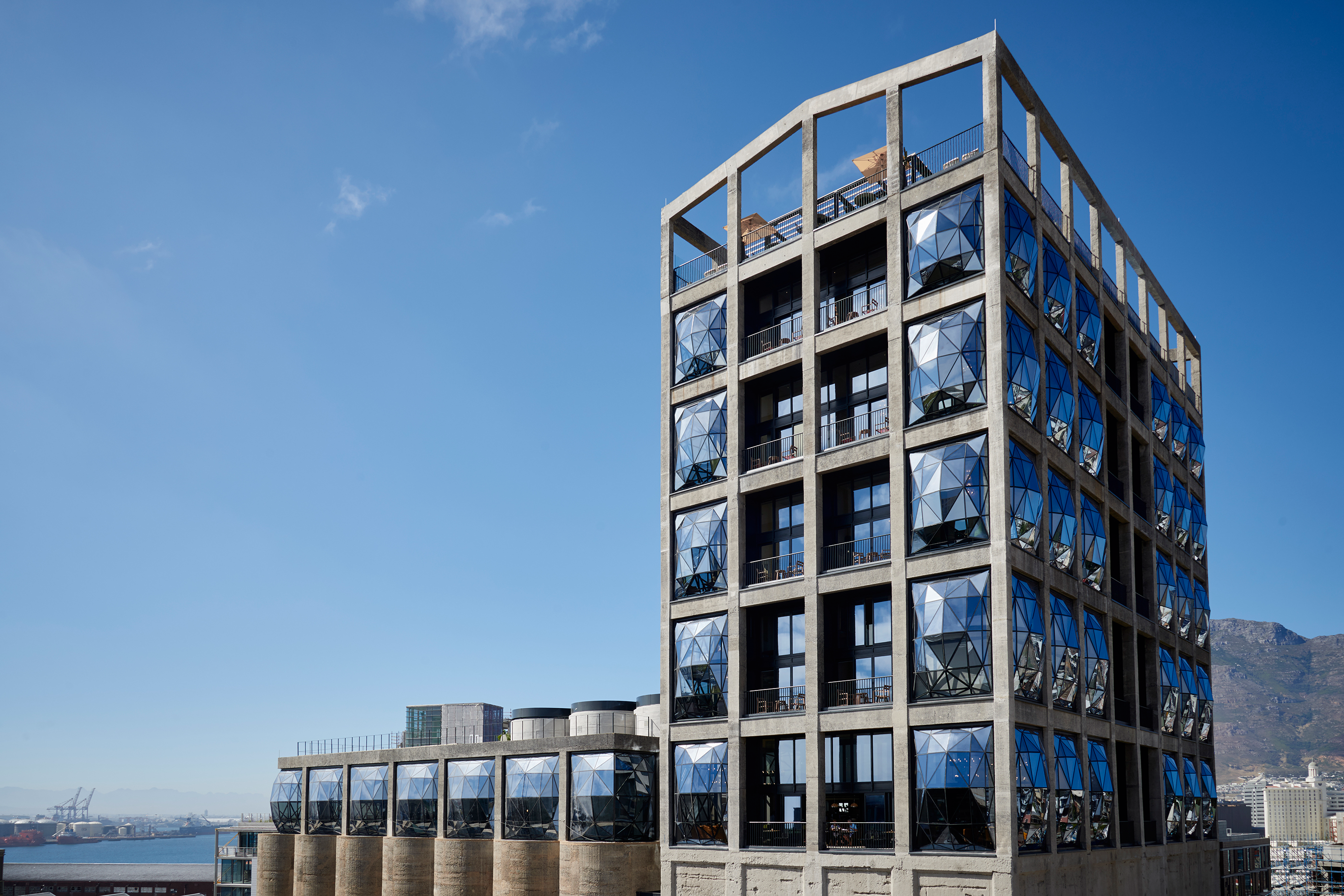 Exterior view of The Silo Hotel in Cape Town featuring iconic geometric glass windows and harbor backdrop under clear blue sky.