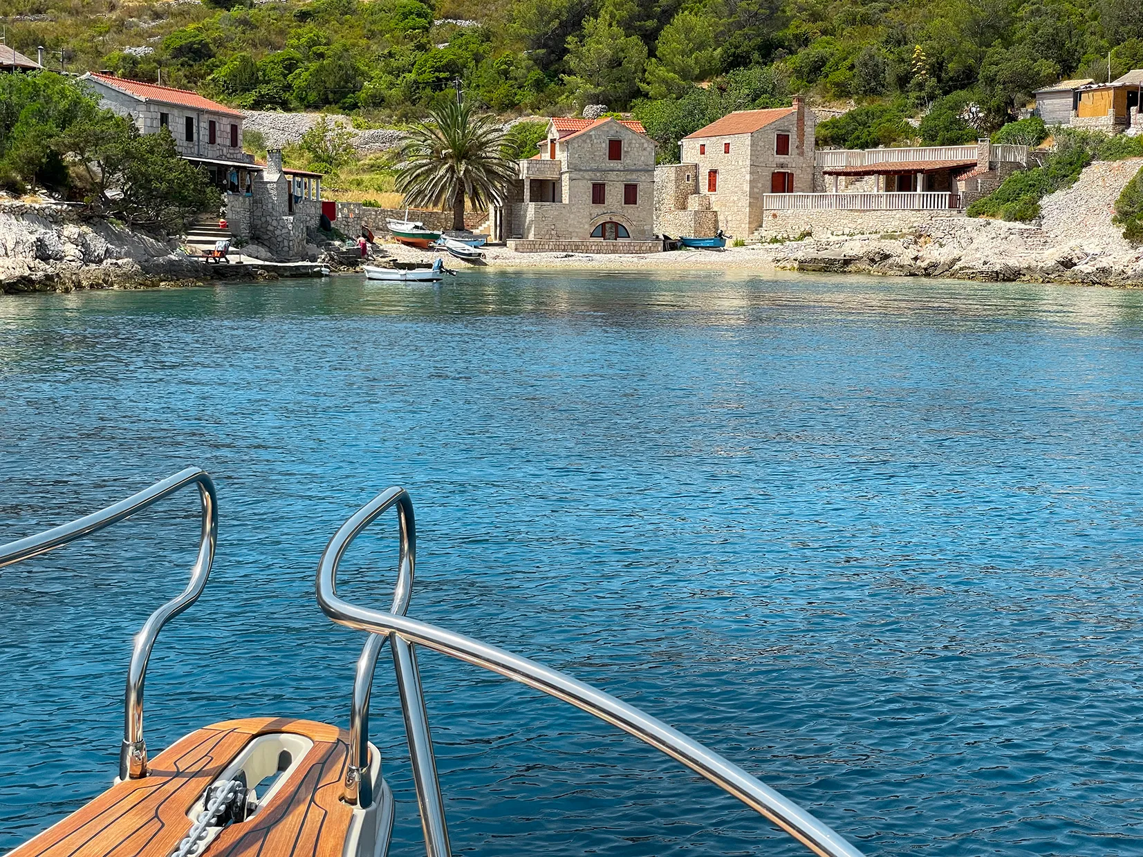 Stone waterfront houses and small boats viewed from a boat in a sheltered bay.