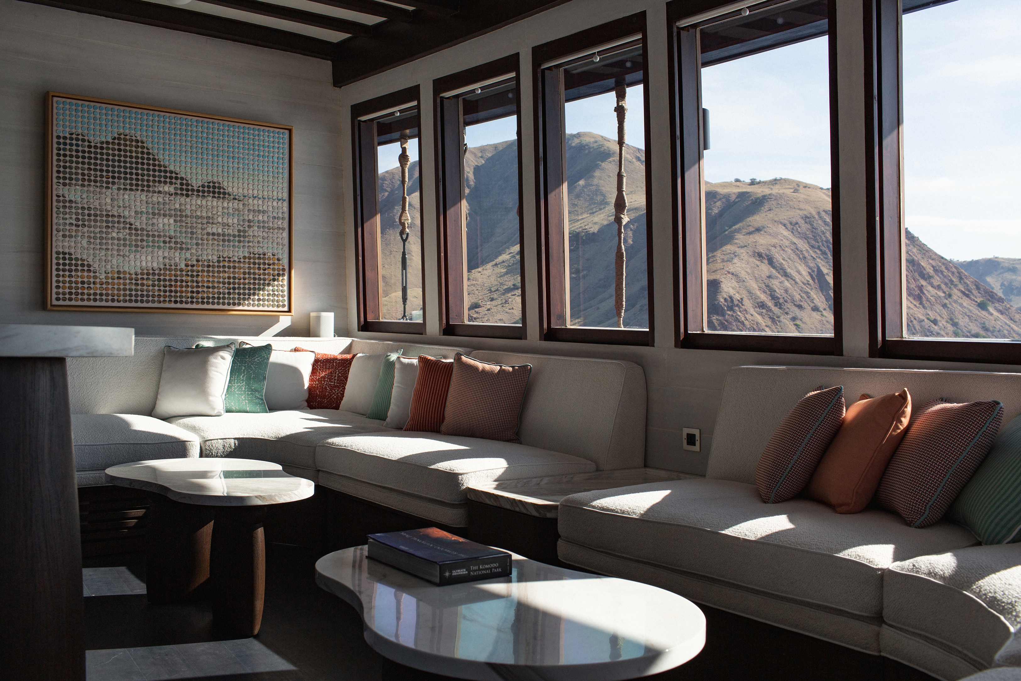 The comfy main saloon of Vela yacht with pale furnishings, colourful cushions and large windows