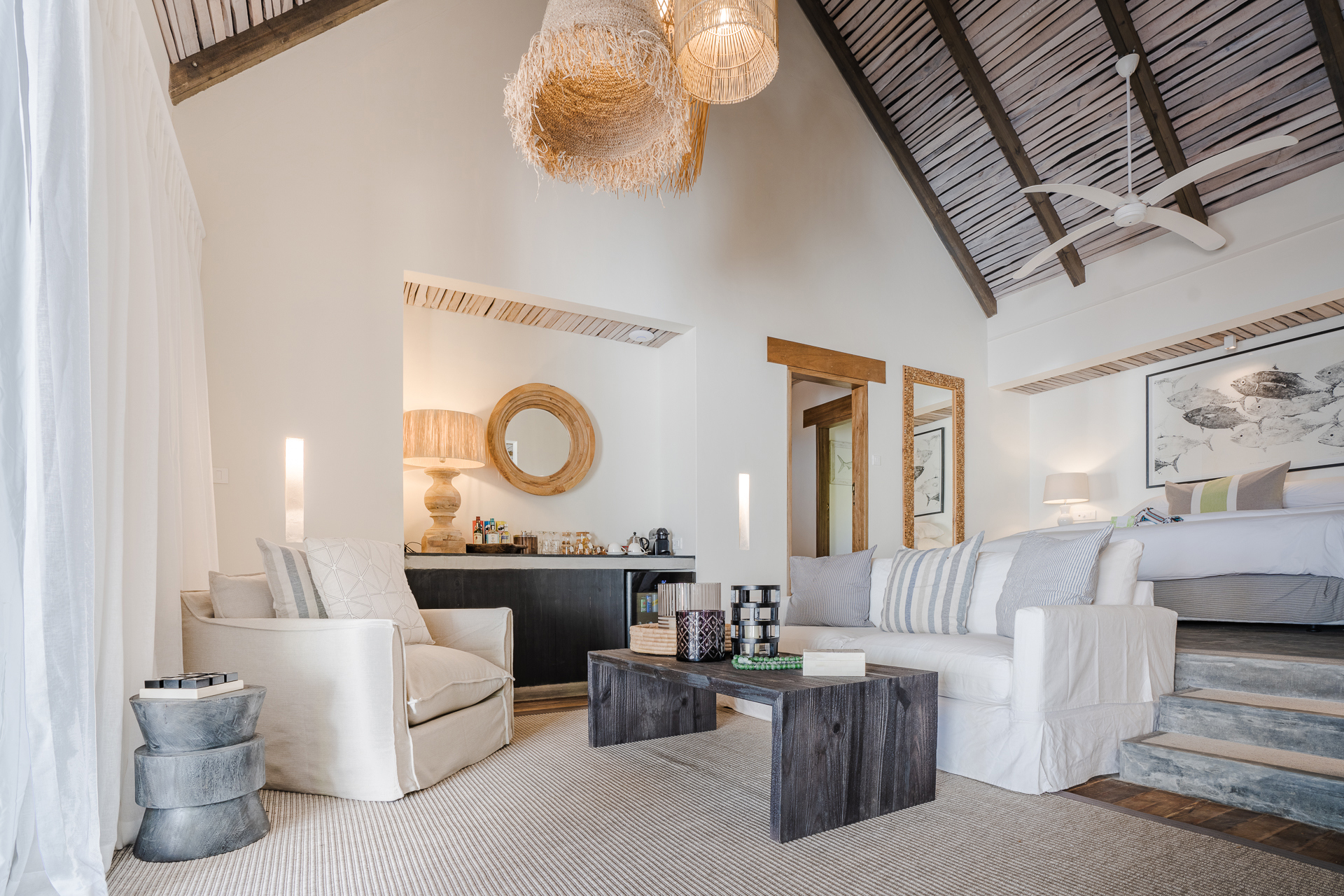 A large airy room with rattan furnishings featuring a plush seating area and bed on a platform