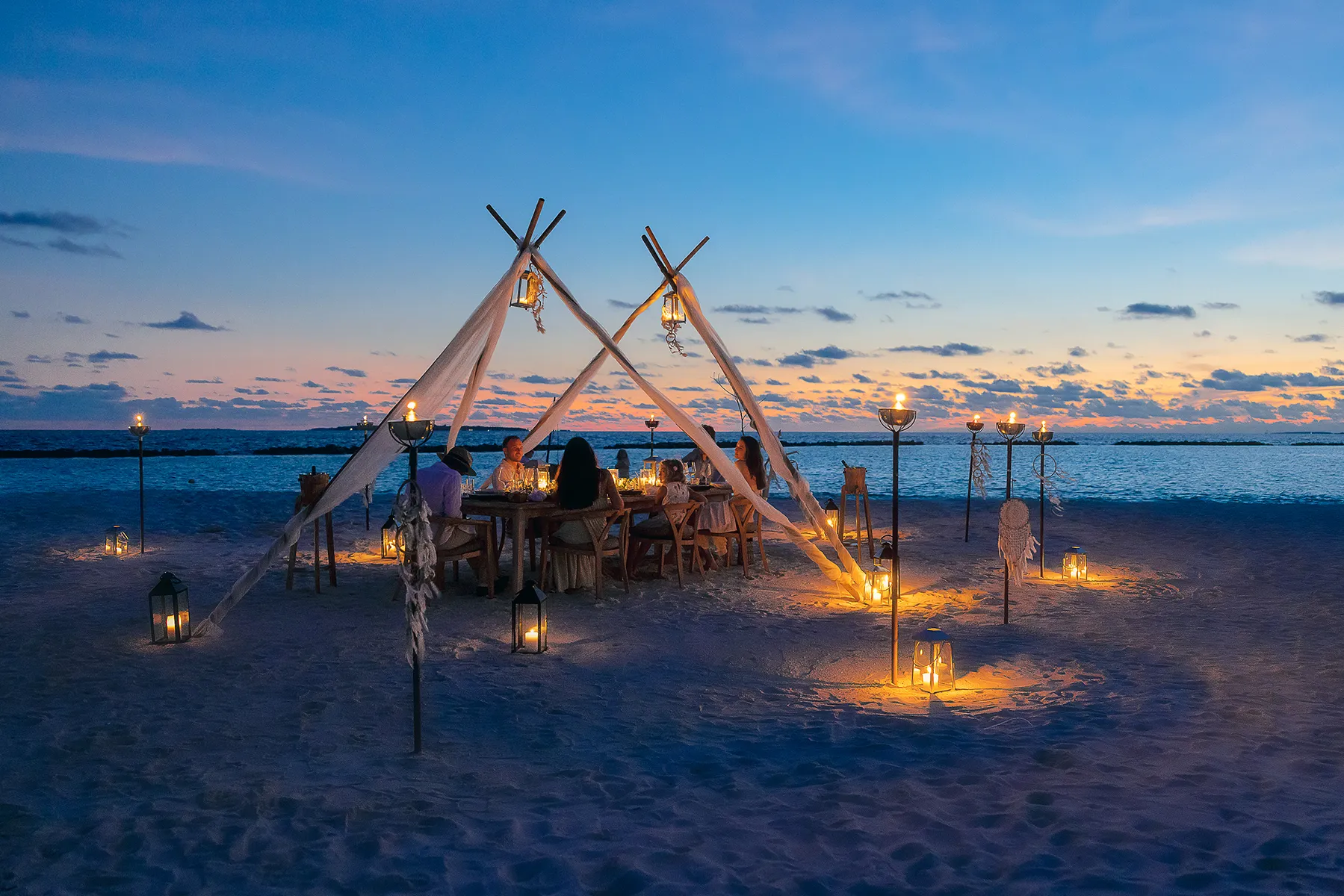 Romantic beach dinner setup at sunset at The Nautilus in the Maldives with lanterns, ocean view, and intimate dining experience.
