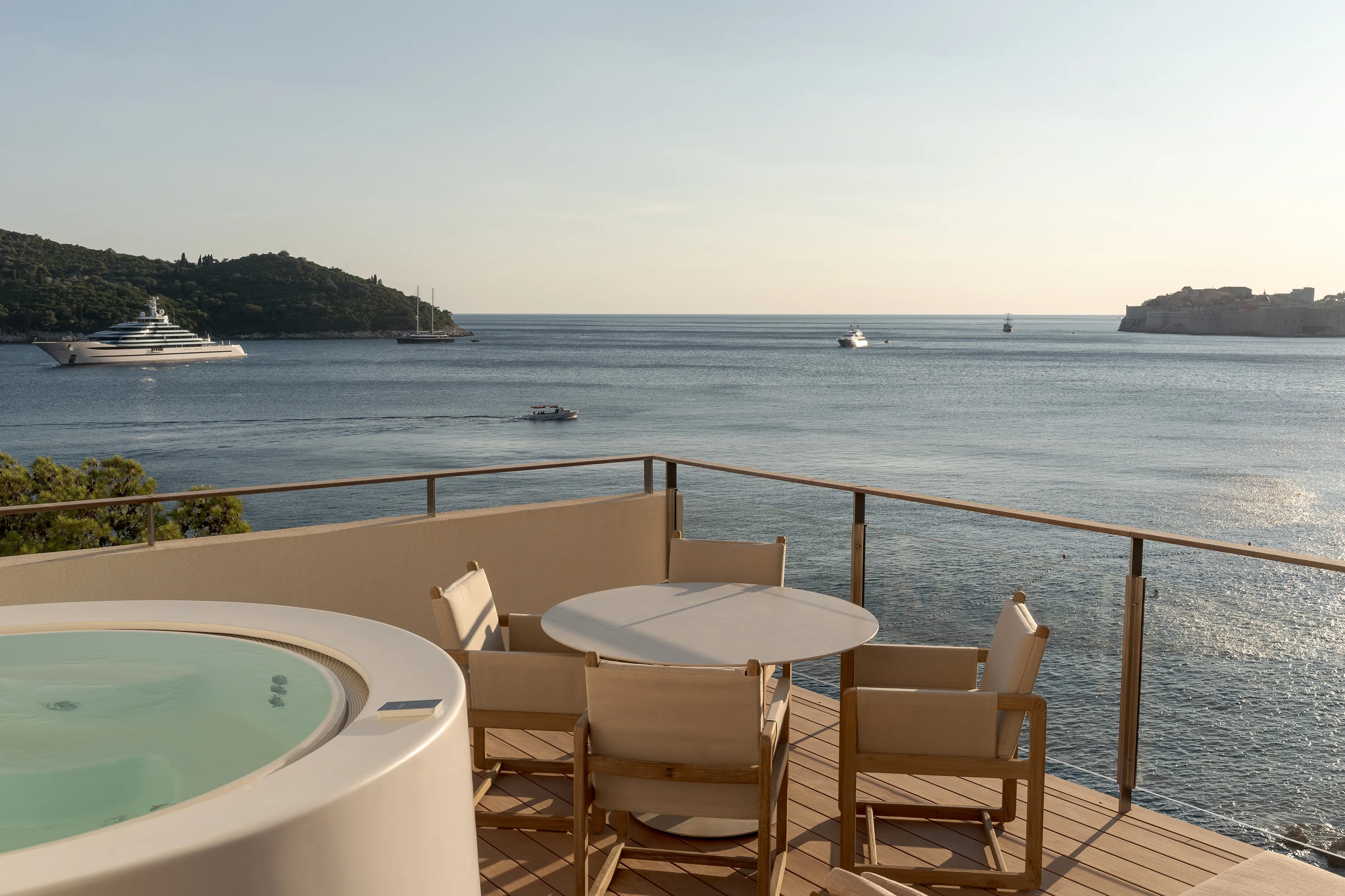 Balcony of Mirakul Suite at Villa Dubrovnik in Croatia featuring a Jacuzzi and dining table and chairs, with sweeping views of the sea, yachts, and Lokrum Island