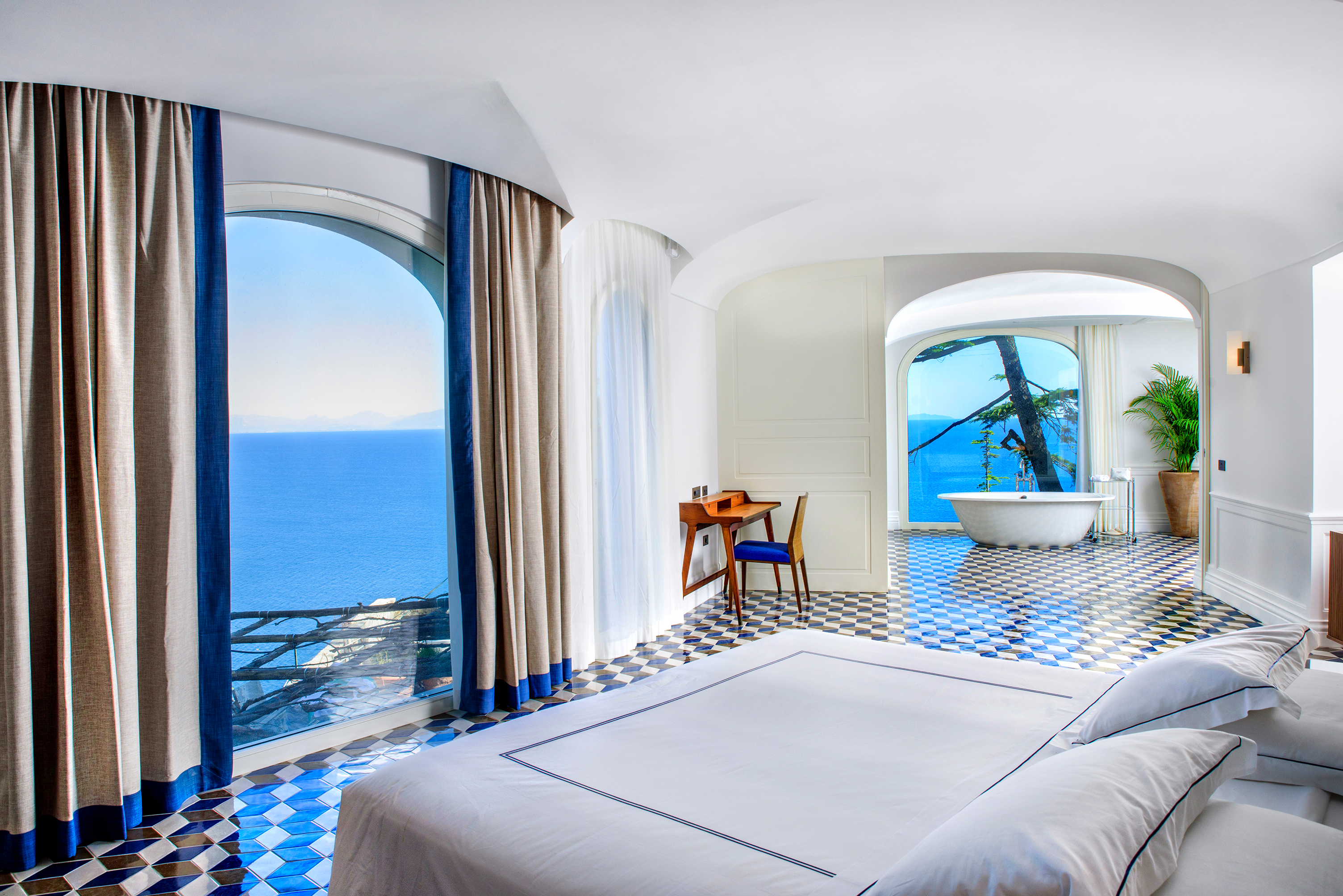Elegant corner suite at Borgo Santandrea in Amalfi featuring a freestanding bathtub, refined decor, and breathtaking ocean views through panoramic windows.