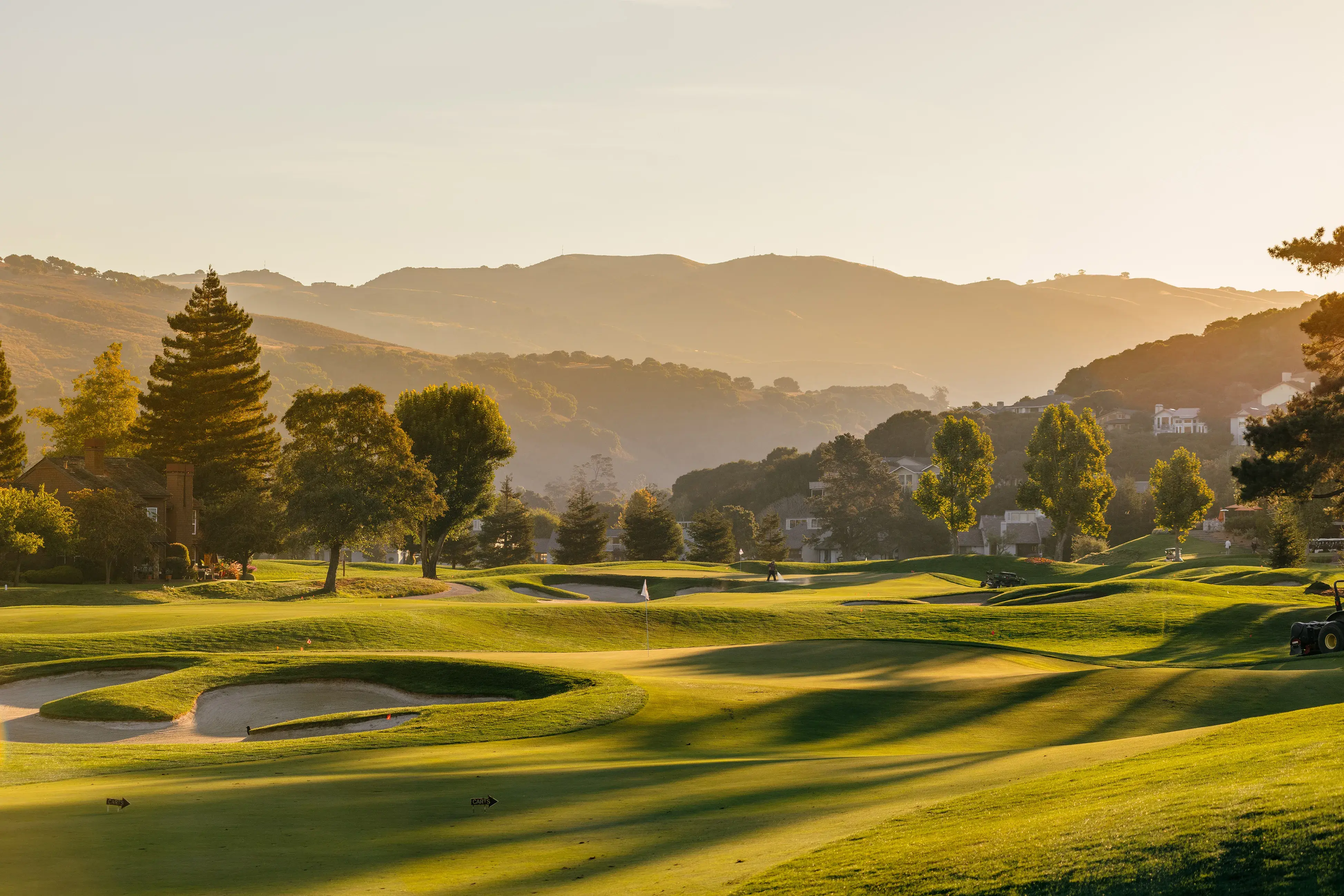 The golf course at Carmel Valley Ranch in California at sunset with a well-kept course backed by trees and hills at sunset