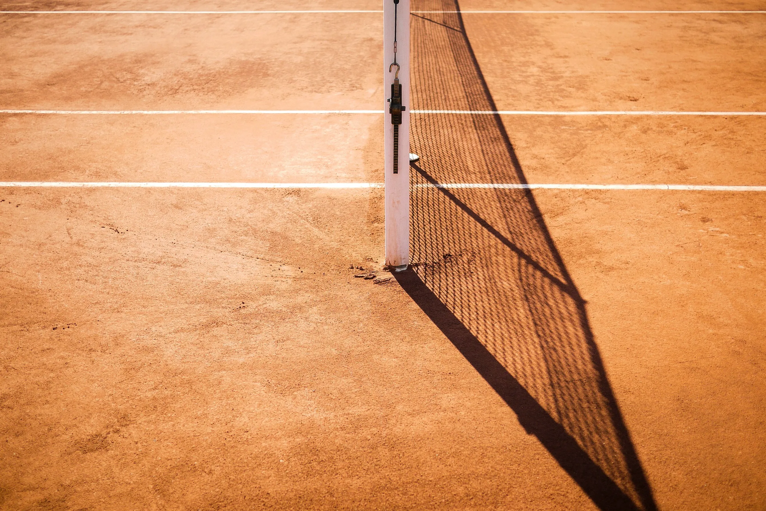 Close-up of a clay tennis court with net casting a shadow across the surface.