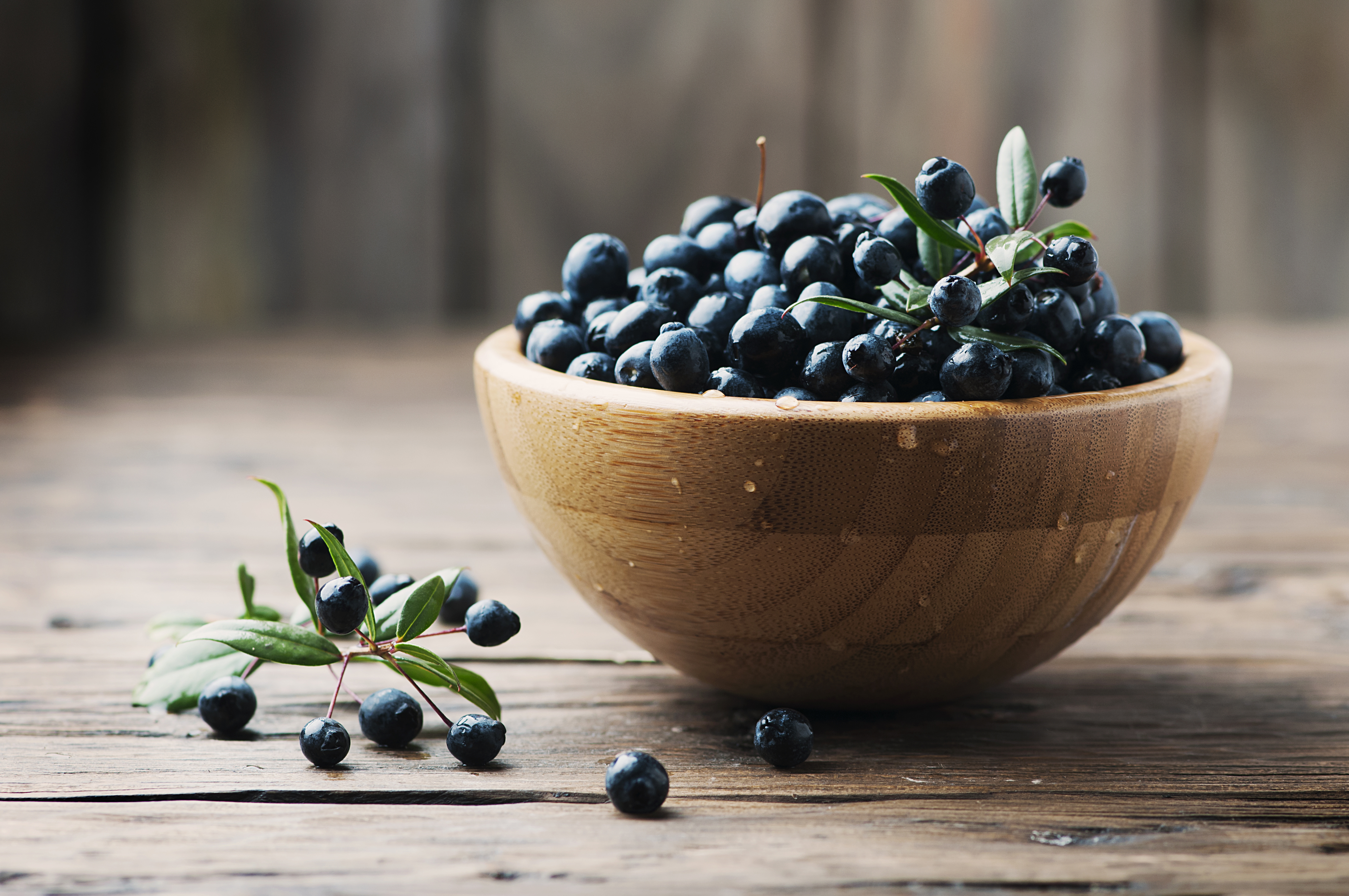 A wooden bowl full of dark myrtle berries with some spilling onto a wooden table