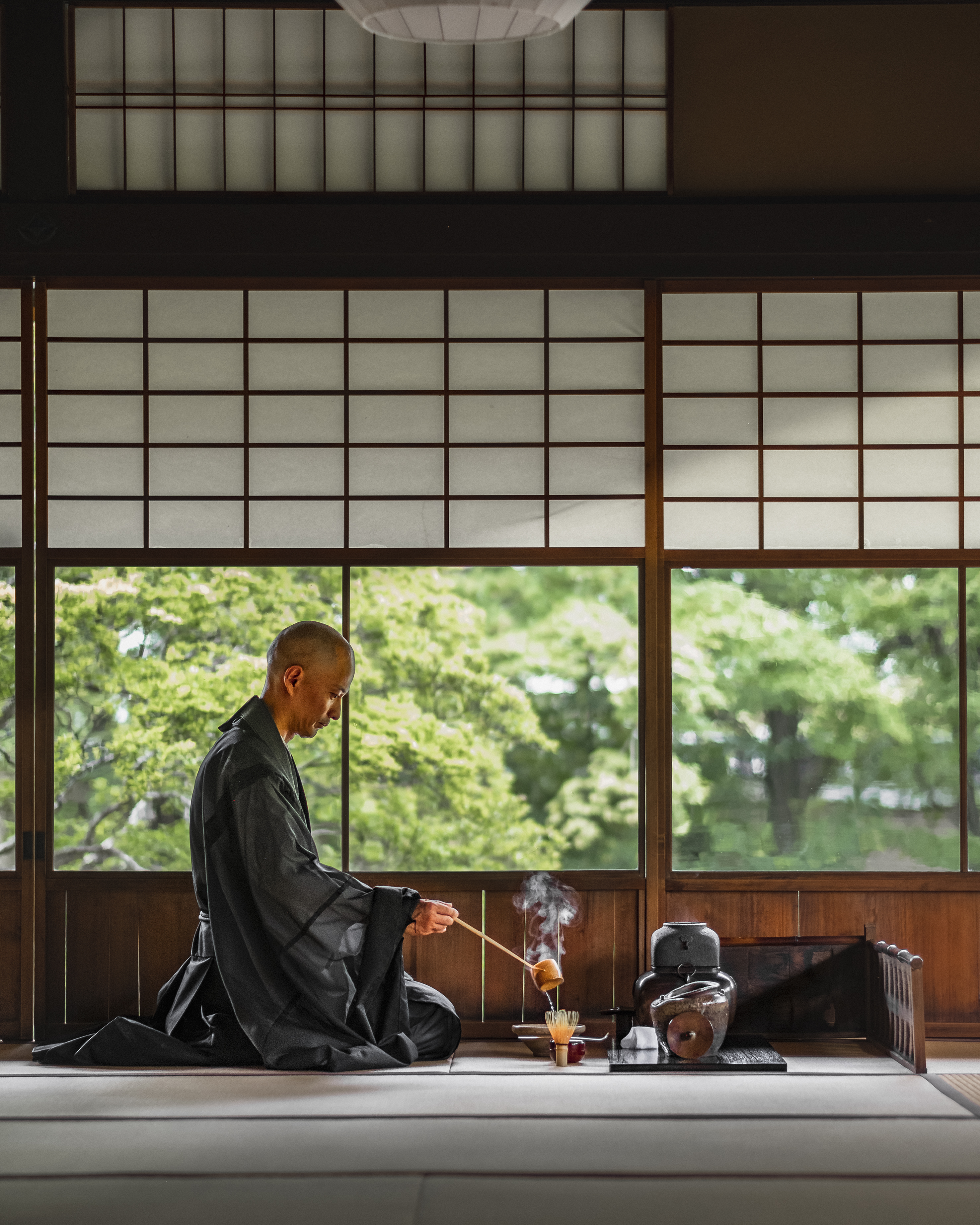 A man wearing a dark kimono making Japanese tea in a traditional building 