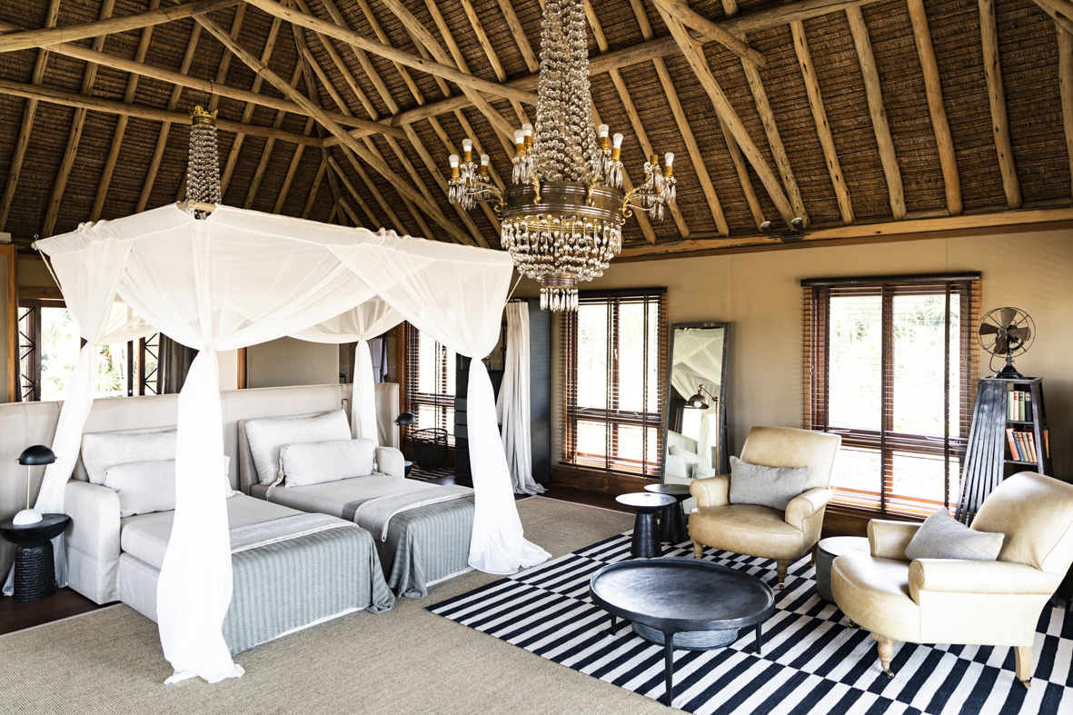 A large vaulted bedroom featuirng a chandelier, twin beds, and a comfy seating area with sofas and striped rug