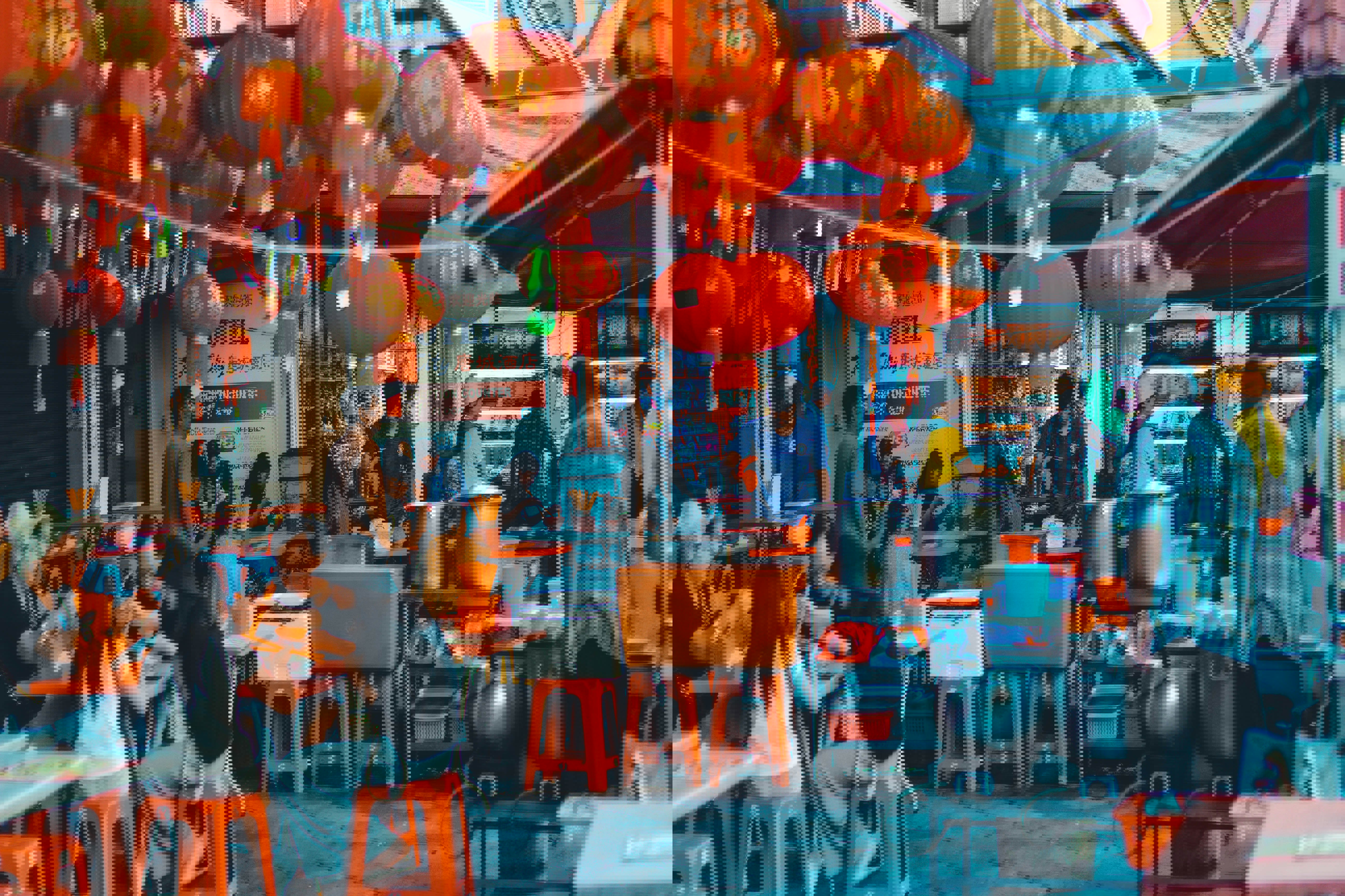 An outdoor food destination in Kuala Lumpur with diners eating on red stools below lanterns