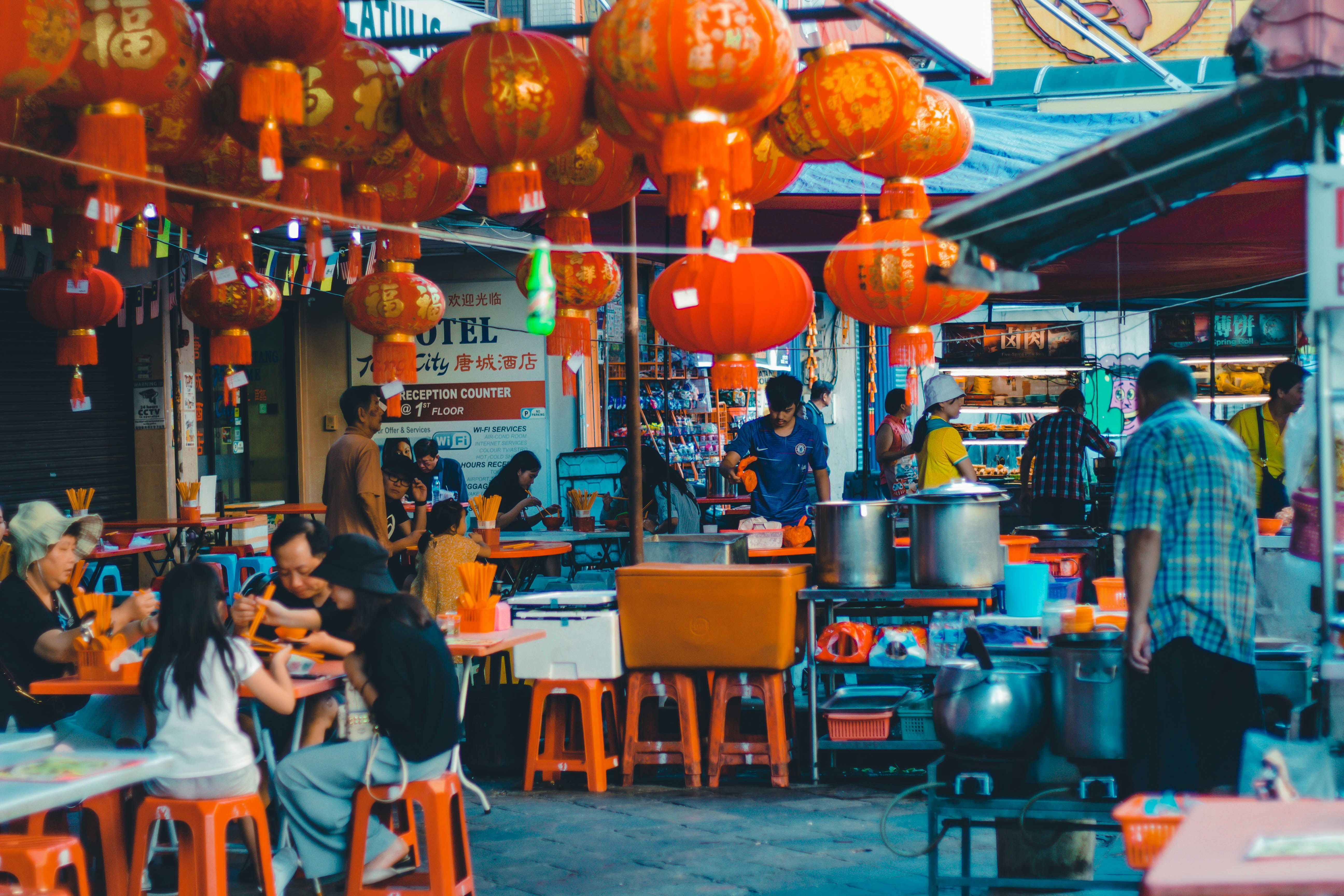 An outdoor food destination in Kuala Lumpur with diners eating on red stools below lanterns