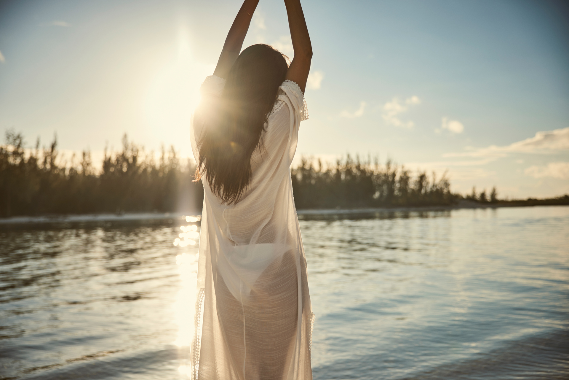 woman stretching with her arms above her head by the waterside at golden hour