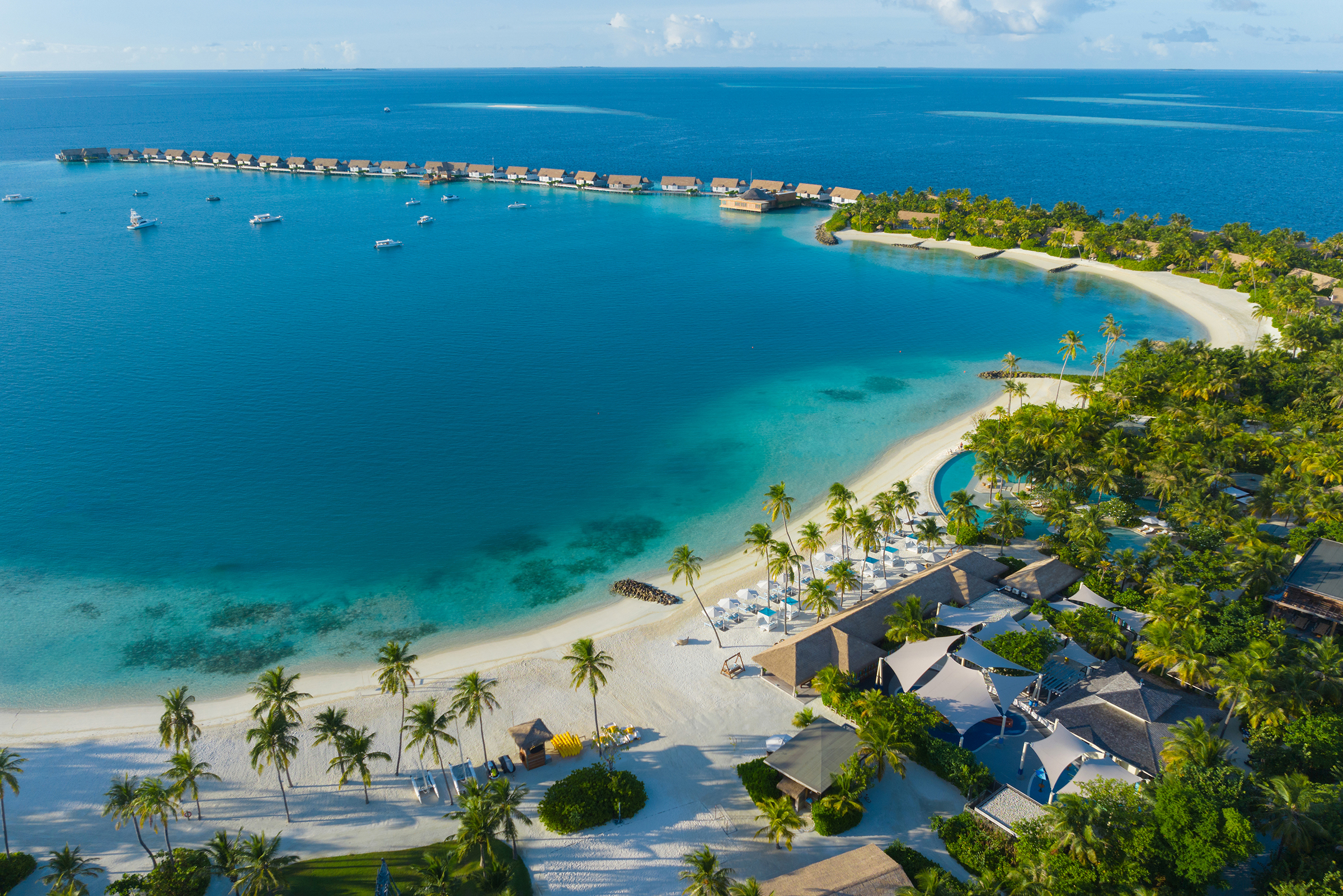 Overview of island with overwater villas curving into the ocean