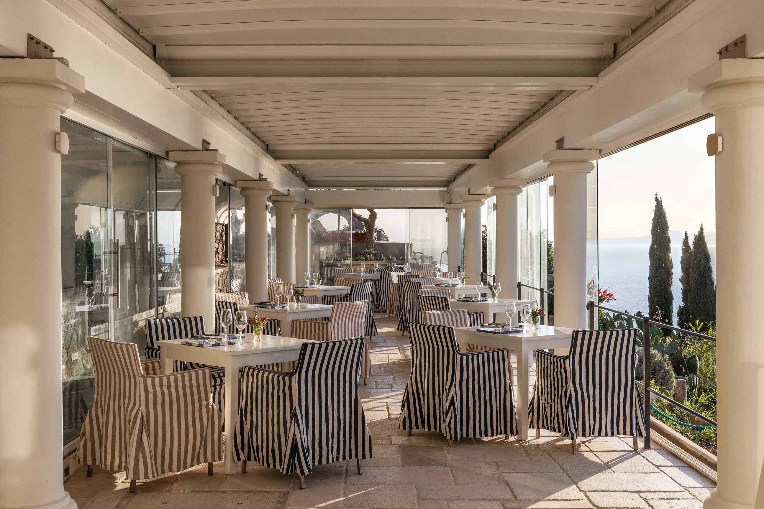 Charming outdoor dining area at San Montano Resort on Ischia with striped chairs, white tables, and a scenic sea view.