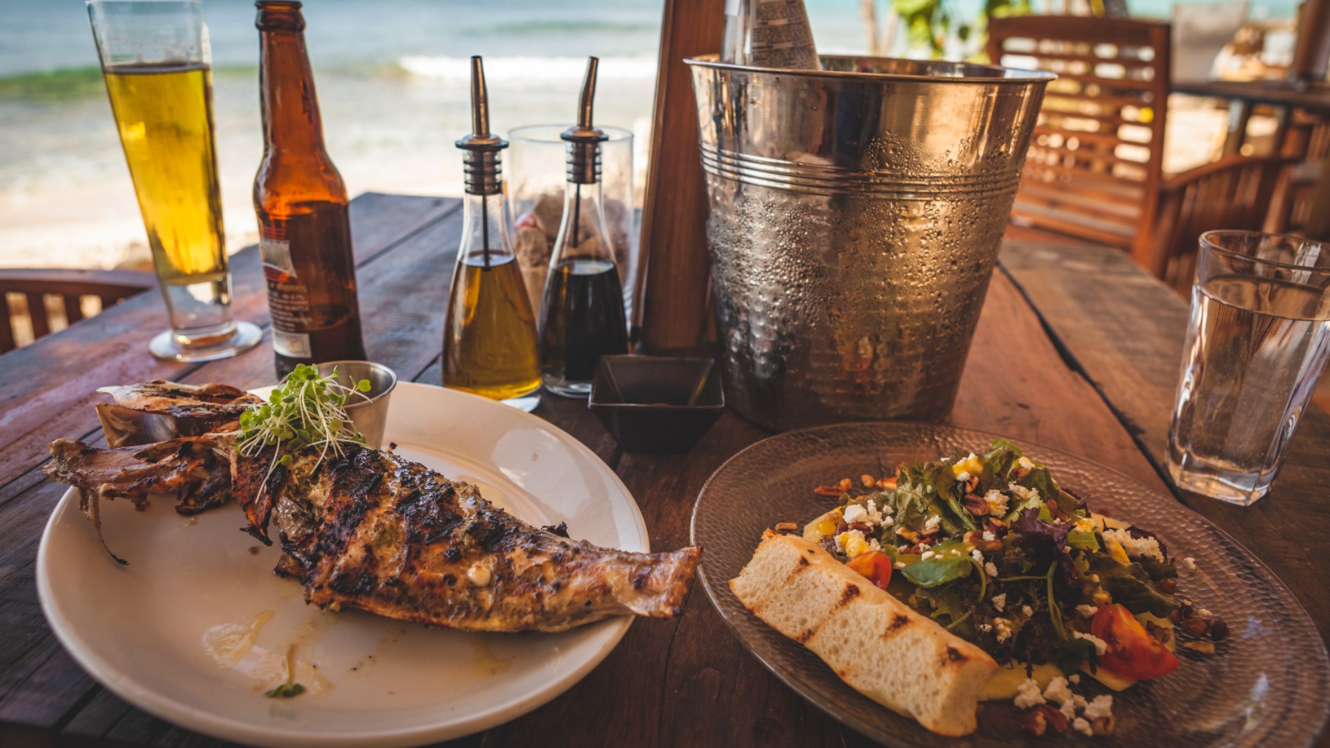 Two plates of food with drinks and condiments on a table by the sea 