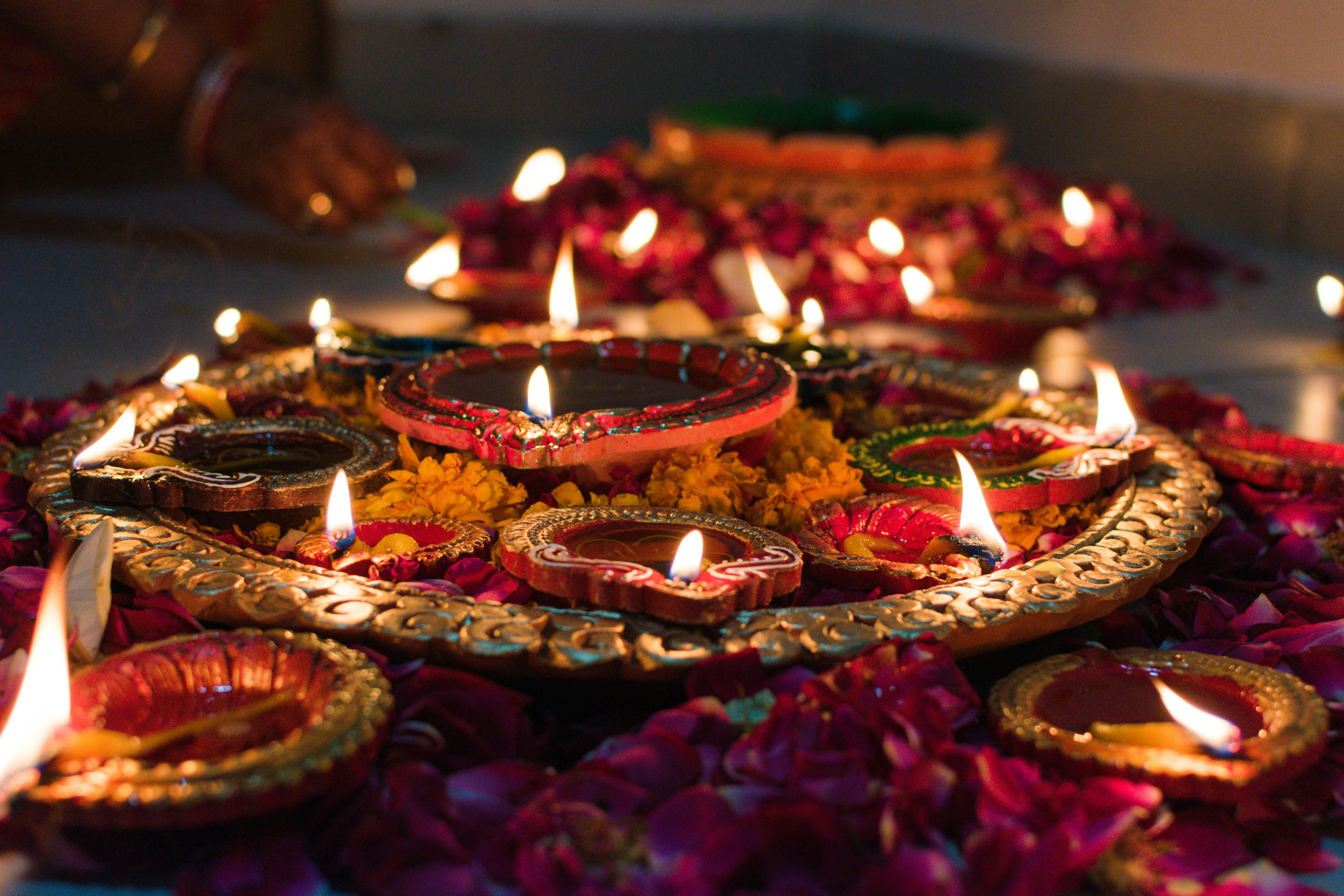 Decorative Diwali diyas arranged on a golden plate surrounded by flower petals, glowing with warm candlelight.