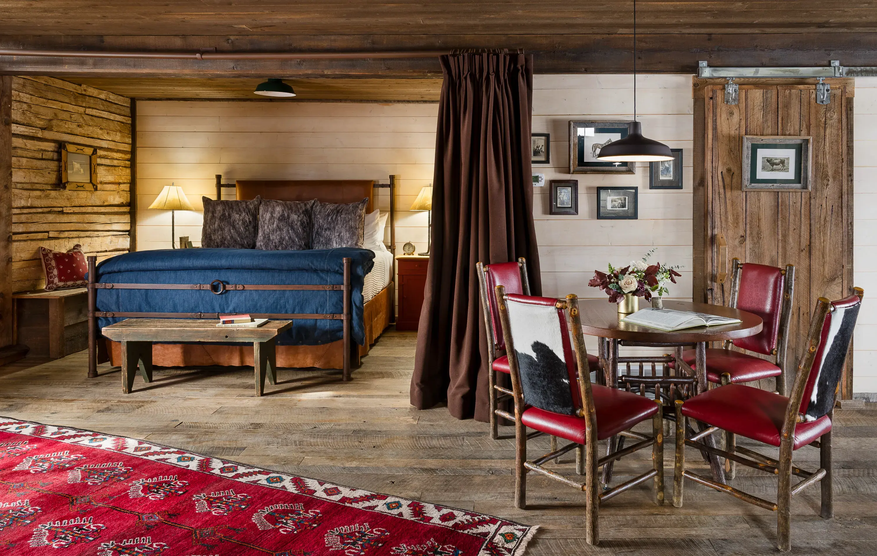 Room in the Stables at The Ranch at Rock Creek in Montana featuring a ranch-style bed and dining table with a patterned rug within wooden cabin walls decorated with western pictures