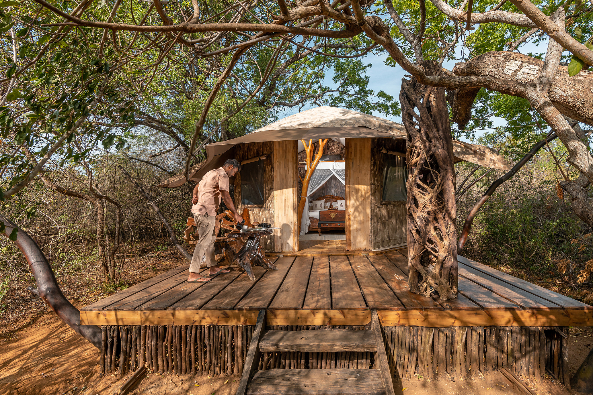 Man setting up a tray outside a thatched hut on a wooden deck
