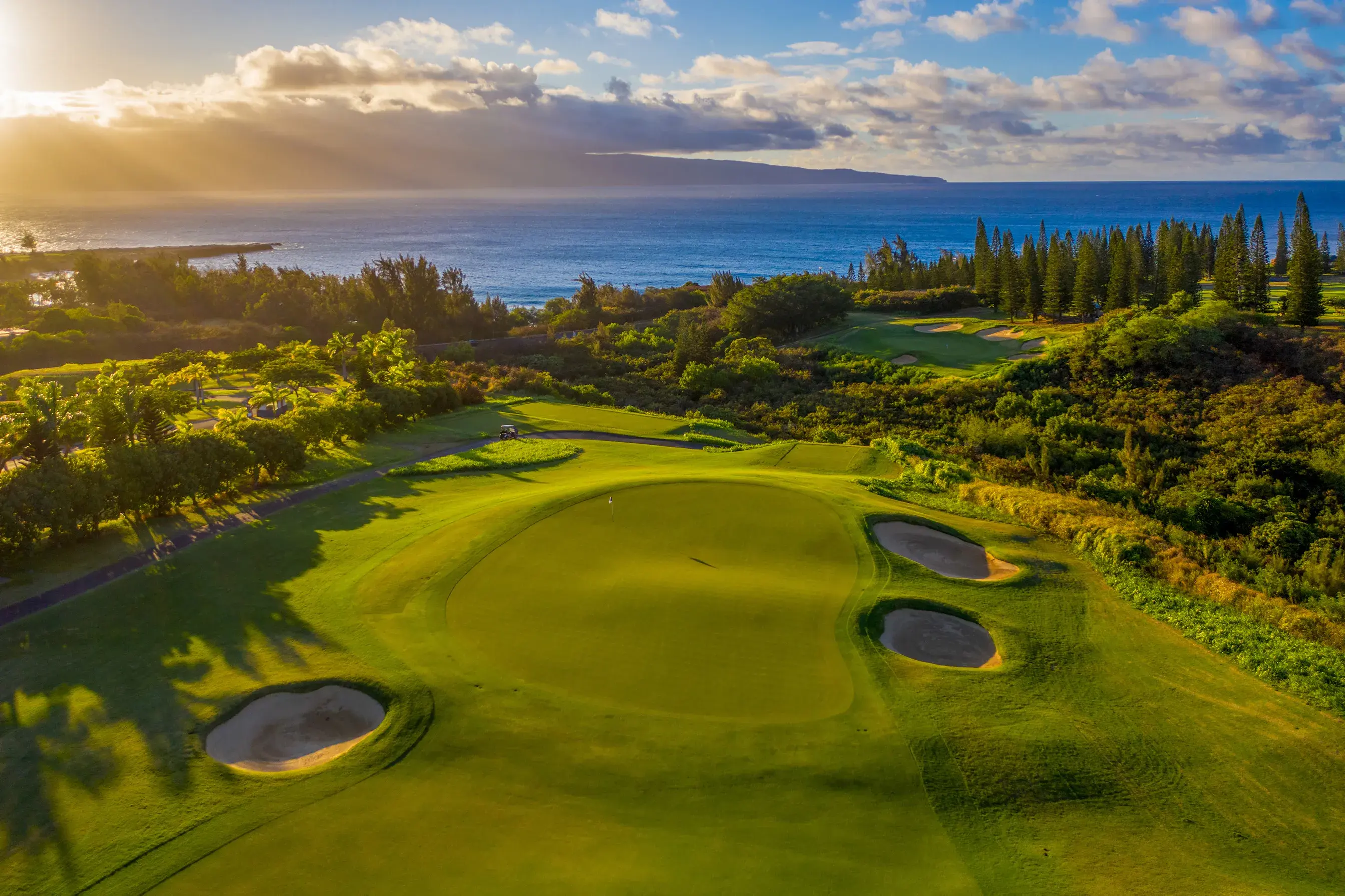 A aerial photo of the golf course near The Ritz-Carlton Maui, Kapalua at sunset with the ocean behind