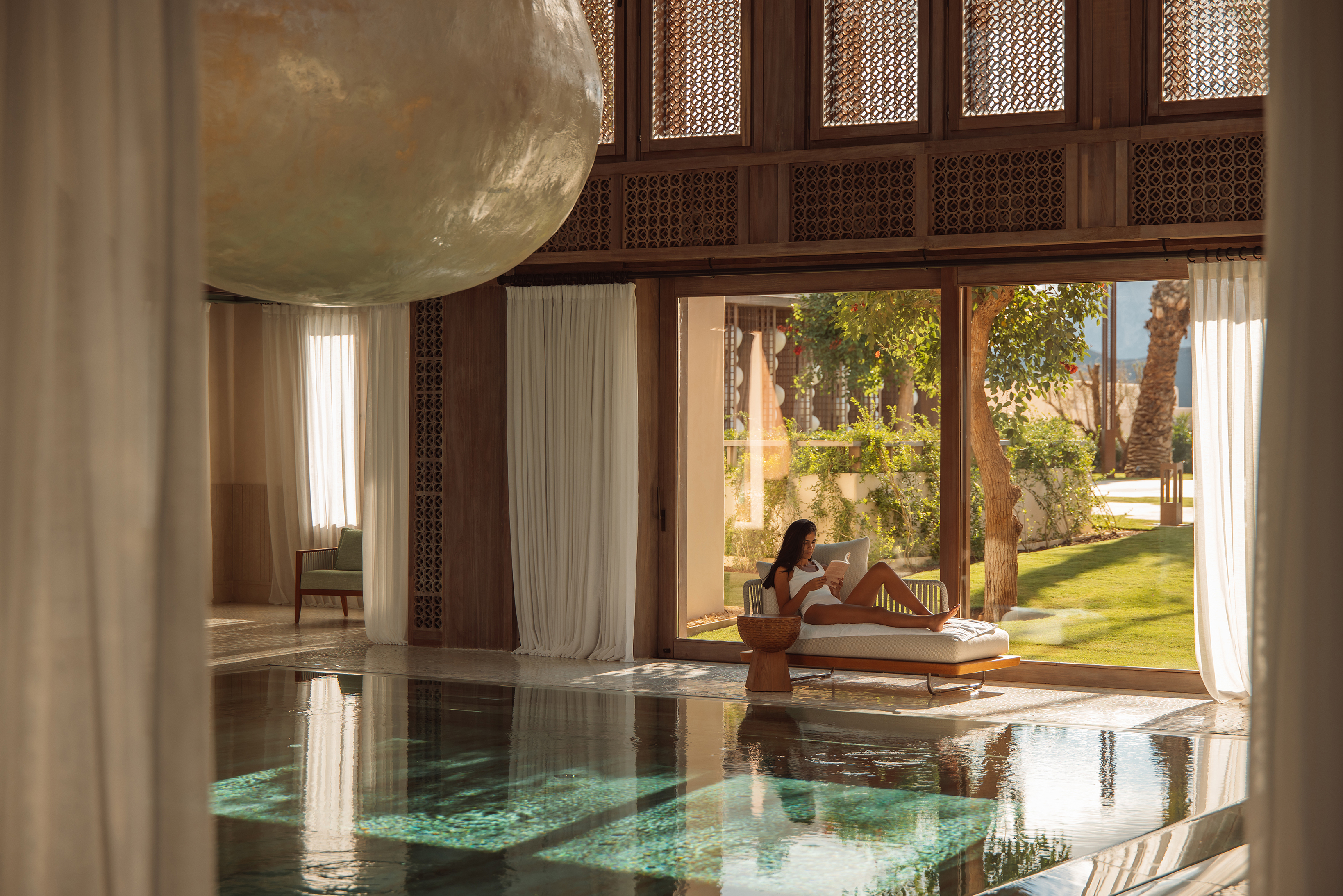 A woman lounging and reading a book by the tranquil quiet pool in the Medi-Spa at Royal Mansour Tamuda Bay