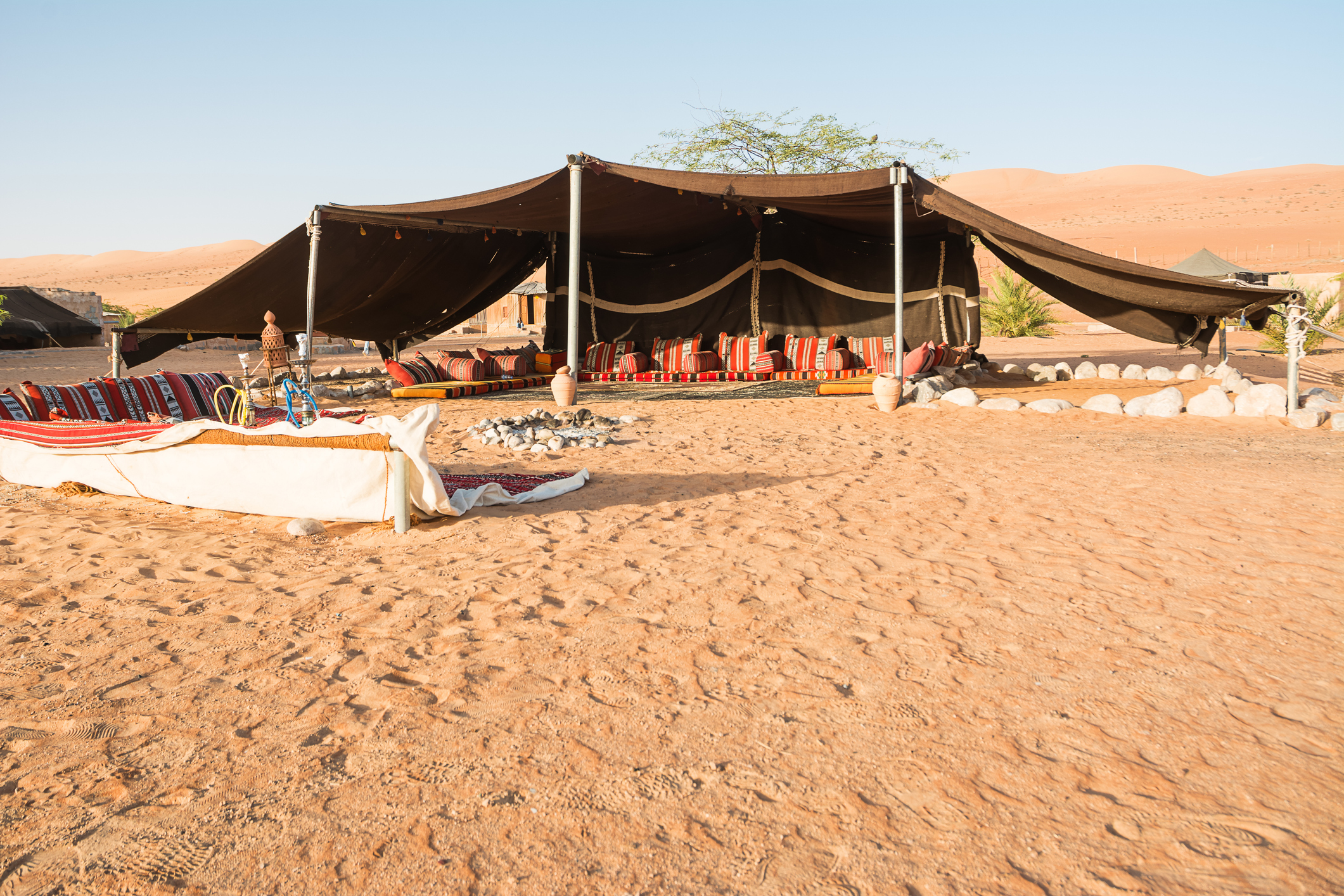 A large black tent with open sides set up in a desert, with colorful cushions and rugs inside and outside at Wahiba Sands Desert Camp, Oman