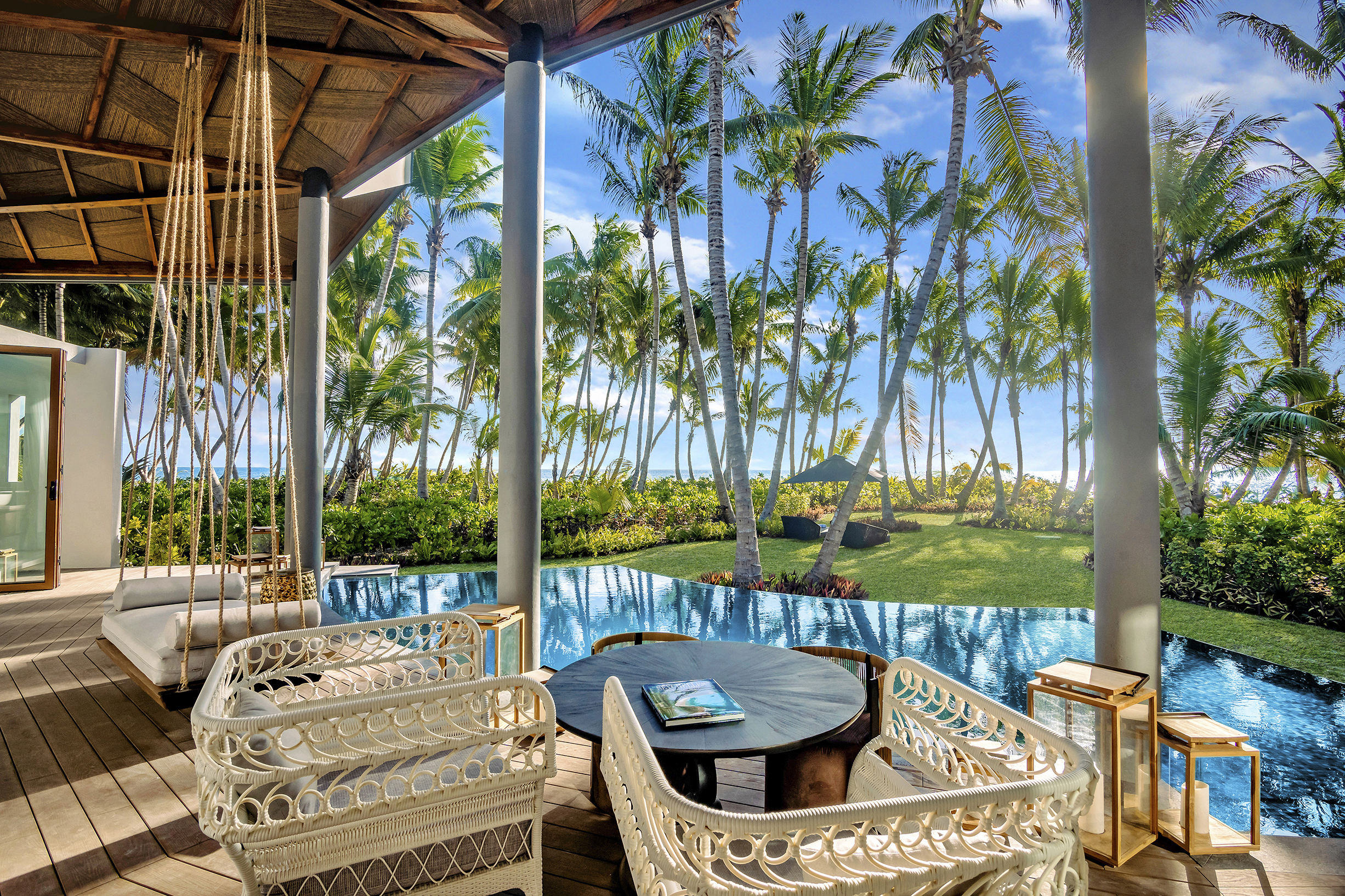 White rattan chairs on a pool villa terrace beside the pool looking out onto a garden of palm trees